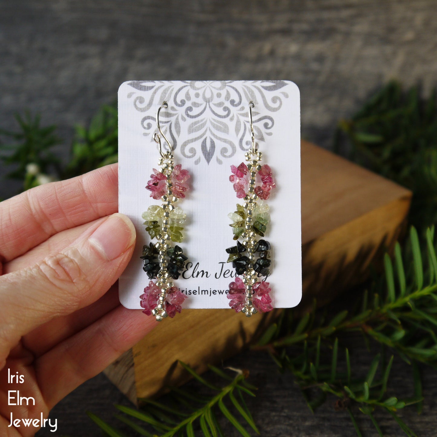 Pair of handmade rainbow tourmaline beadwork earrings on a card held by a hand with a natural background
