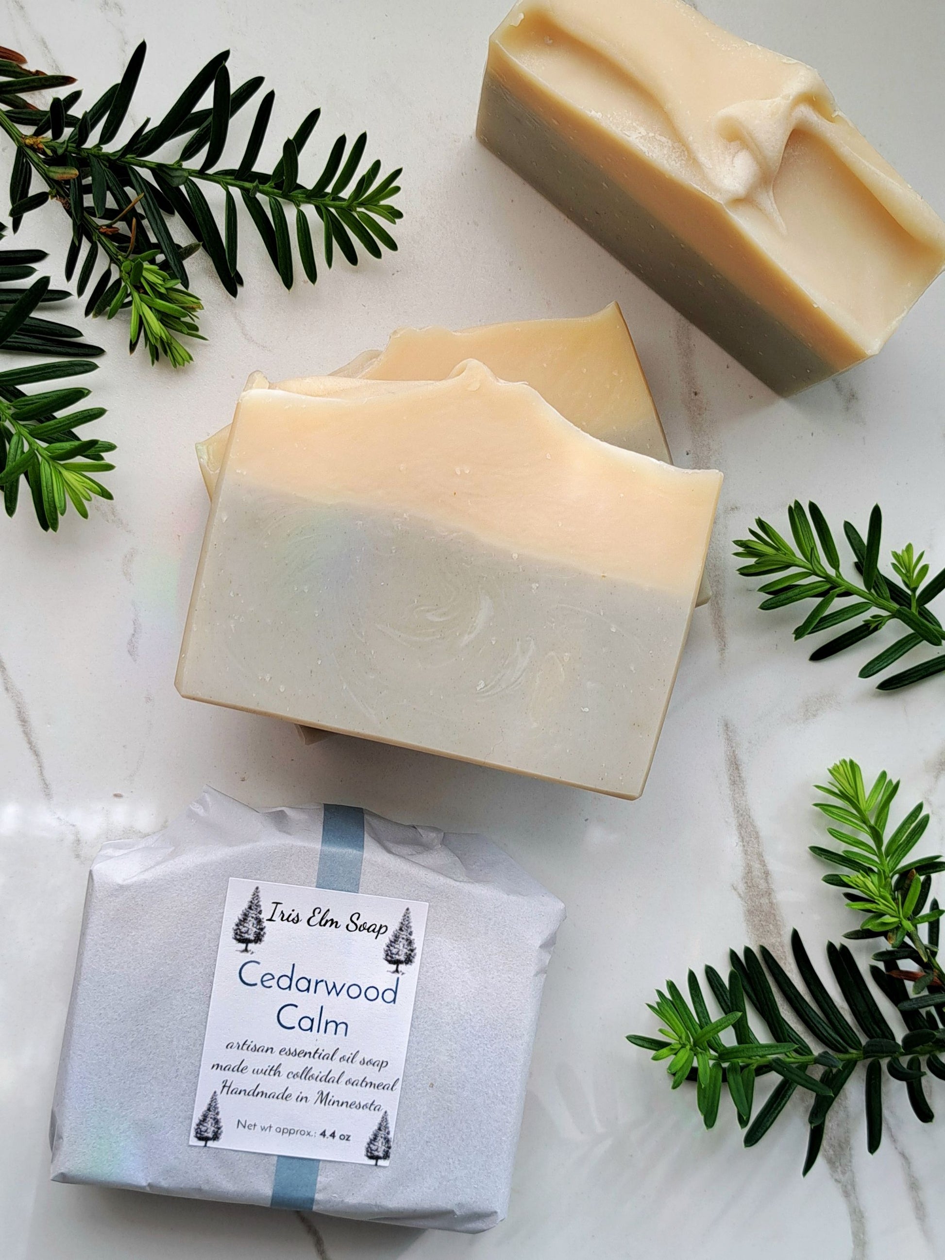 Three bars of soap with a package labeled 'Cedarwood Calm' on a marble surface with greenery.