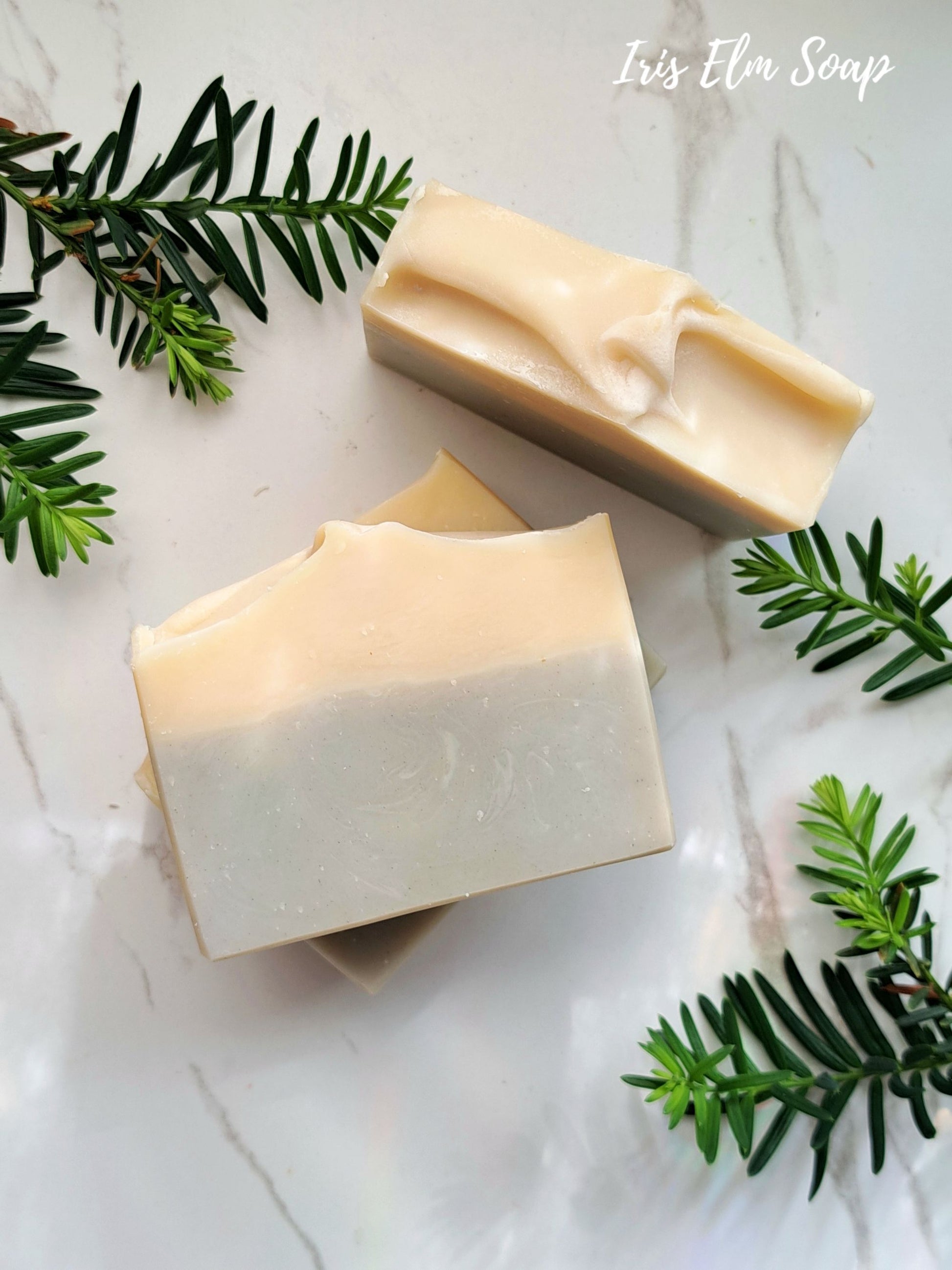 Three bars of cedarwood calm essential oil soap on a marble surface with greenery, featuring 'Iris Elm Soap'.