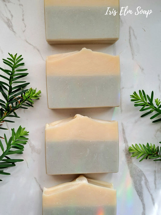 Four bars of cedarwood calm essential oil soap with green leaves on a marble surface, featuring 'Iris Elm Soap'.