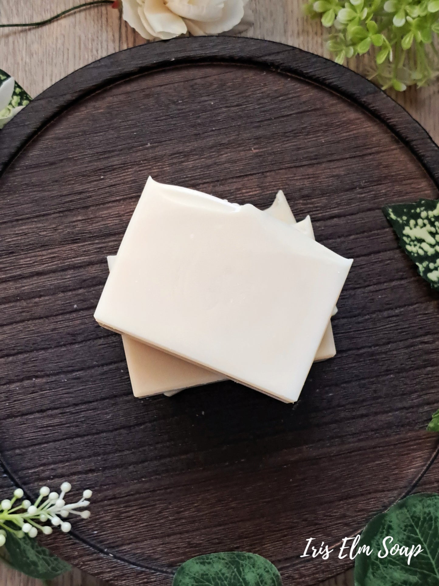 Three bars of unscented handmade soap stacked on a wooden surface with decorative elements.