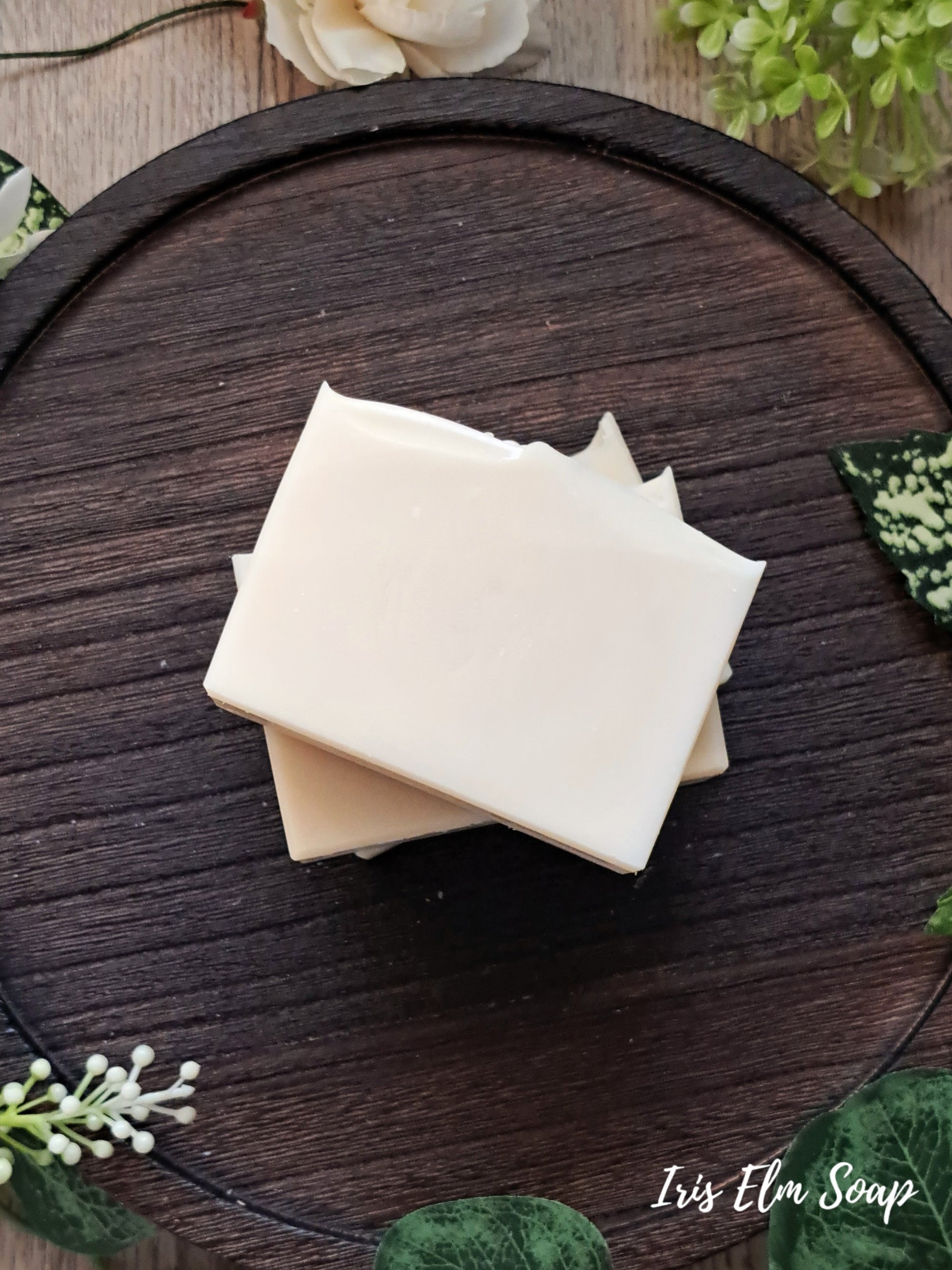 Three bars of unscented handmade soap stacked on a wooden surface with decorative elements.