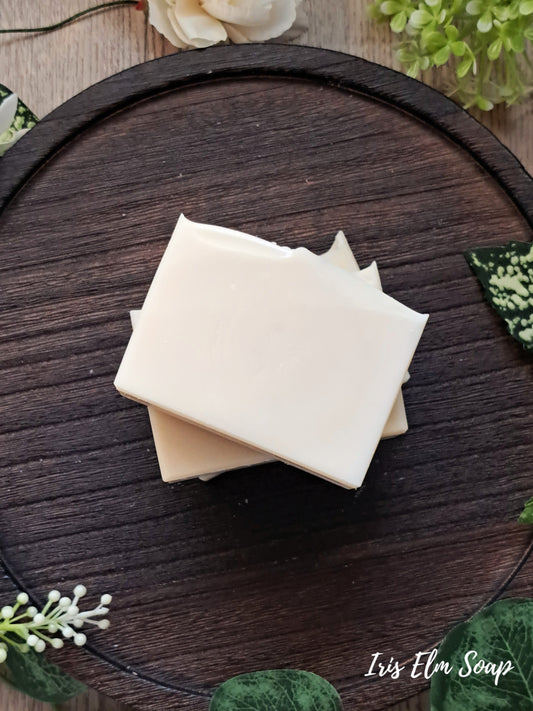 Three bars of unscented handmade soap stacked on a wooden surface with decorative elements.