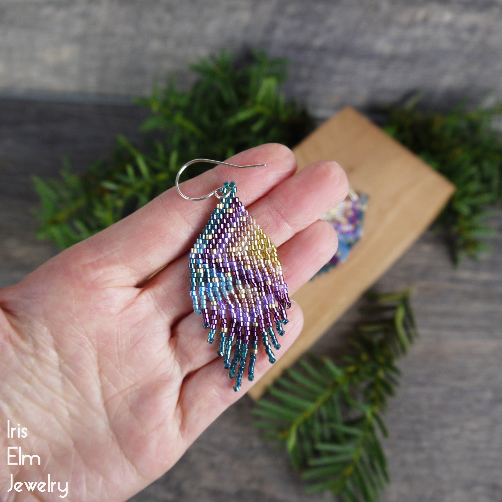 Multicolored fringe seed bead small beaded earring held in a hand with a blurred natural background