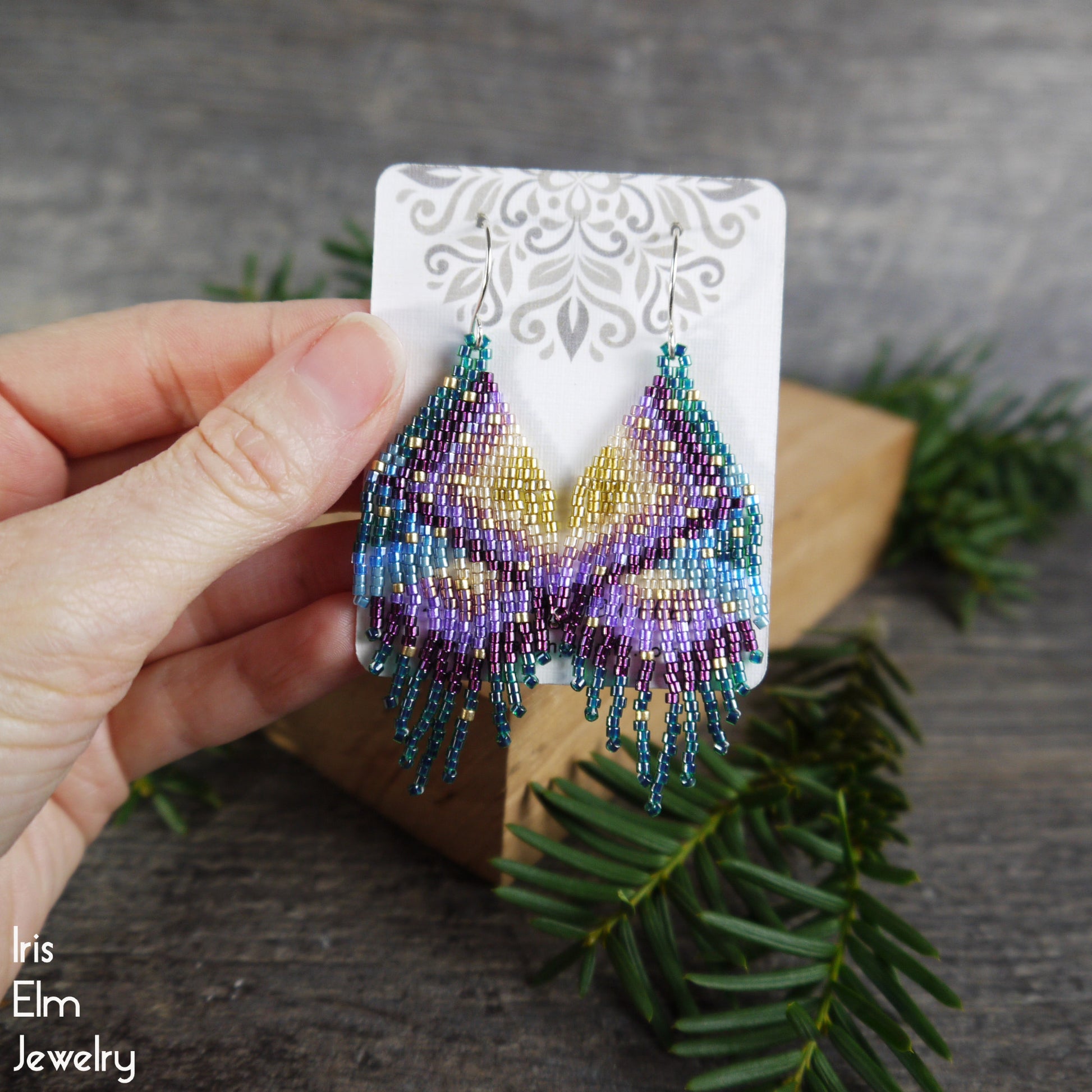 Hand holding beaded seed bead fringe earrings on a card with a natural background