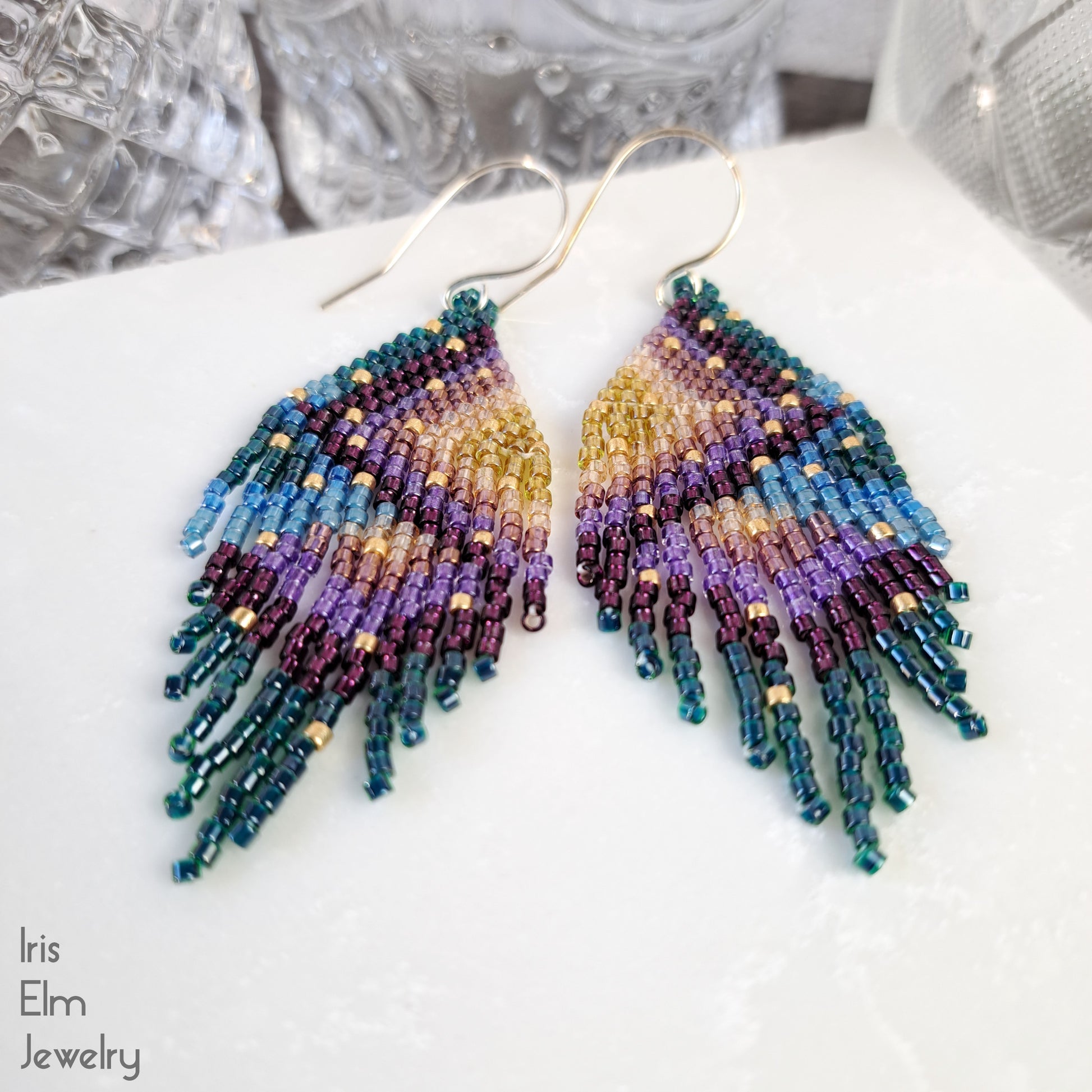 Multicolored beaded rainbow fringe handmade seed bead earrings on a white surface with 'Iris Elm Jewelry' branding.