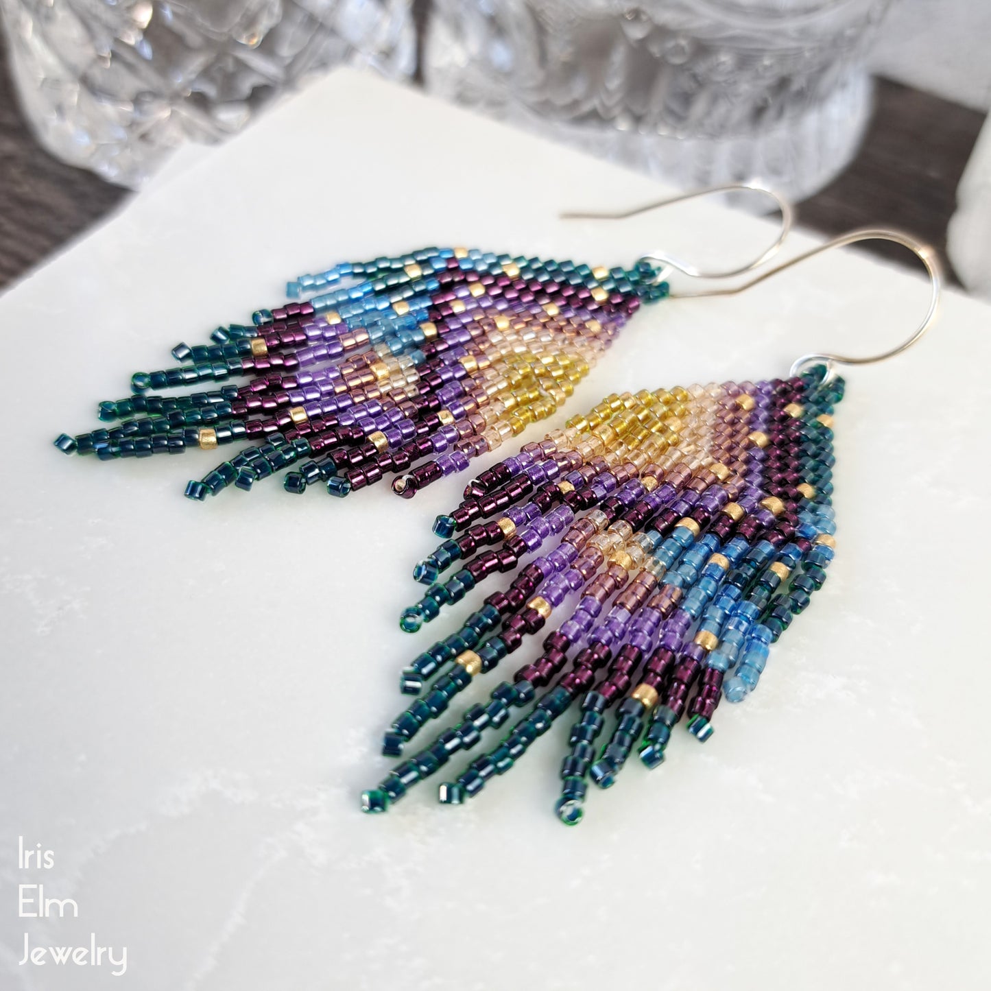 Colorful beadwork gold purple blue green fringe earrings on a white surface with 'Iris Elm Jewelry' branding.