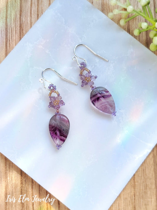 purple amethyst beaded flower and rainbow fluorite leaf gemstone dangle earrings on white marble surface