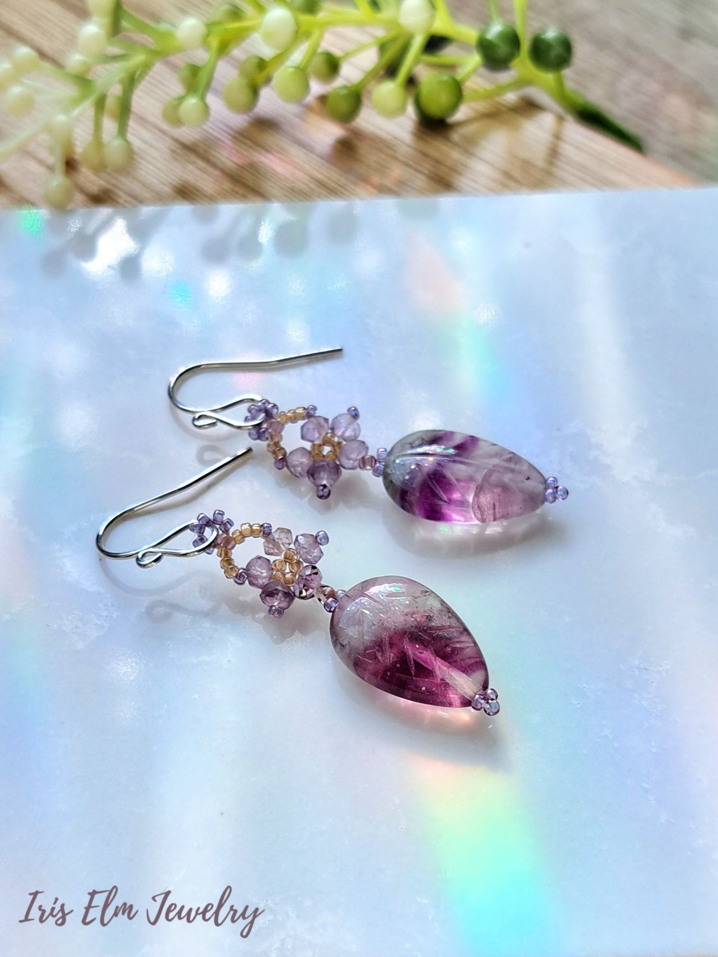 purple amethyst beaded flower and rainbow fluorite leaf gemstone dangle earrings on white marble surface