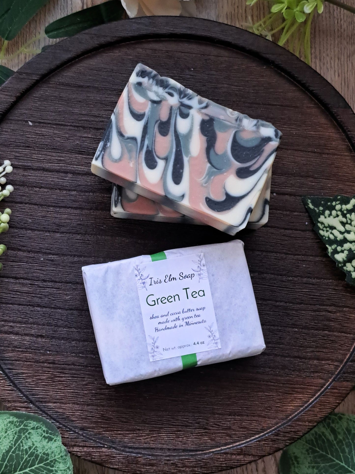 Two bars of handmade soap, one wrapped and one unwrapped, on a wooden surface with green tea soap packaging.