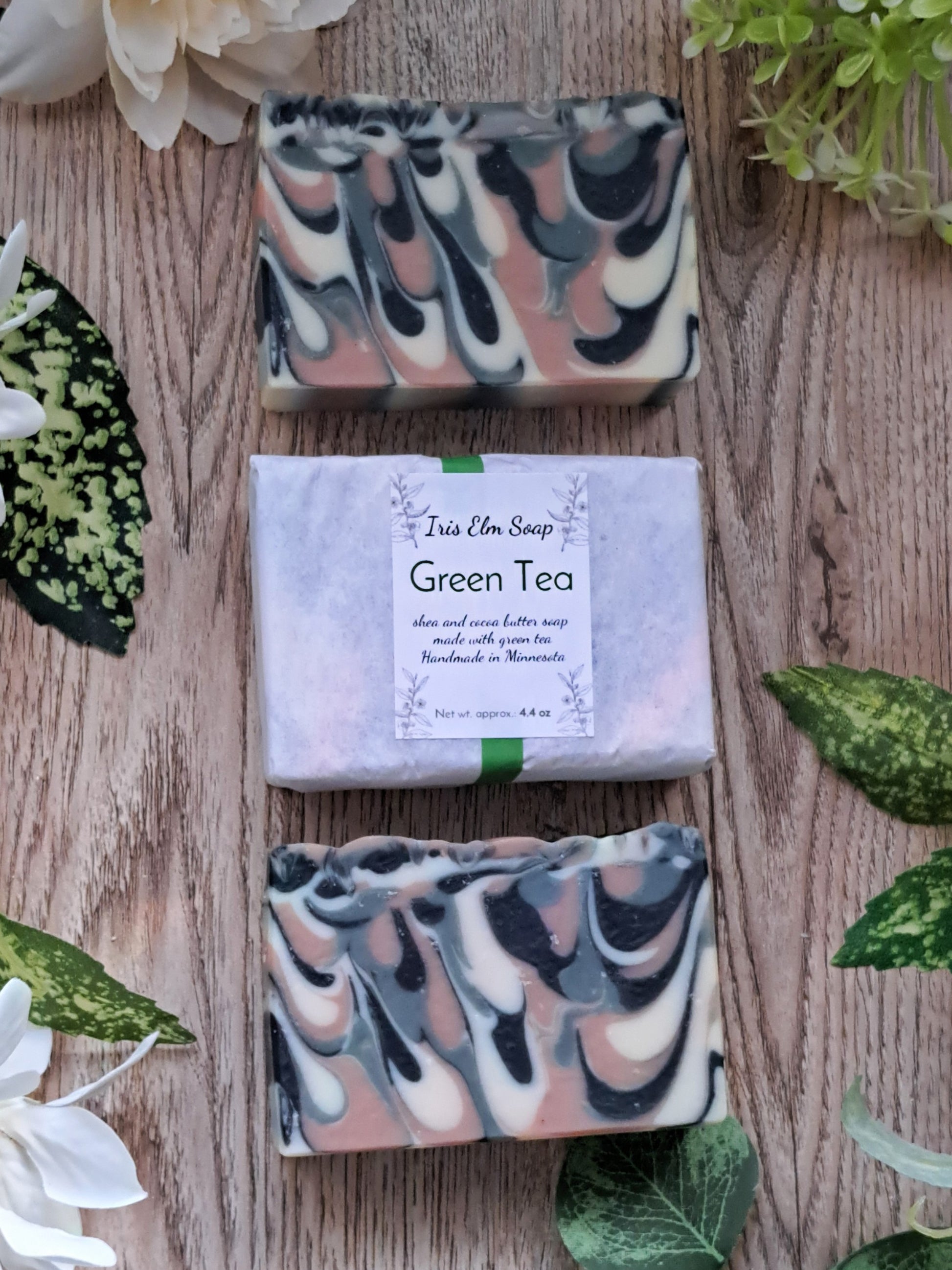 Three bars of artisan handmade cold process soap with 'Green Tea' label on a wooden surface with green leaves and flowers.
