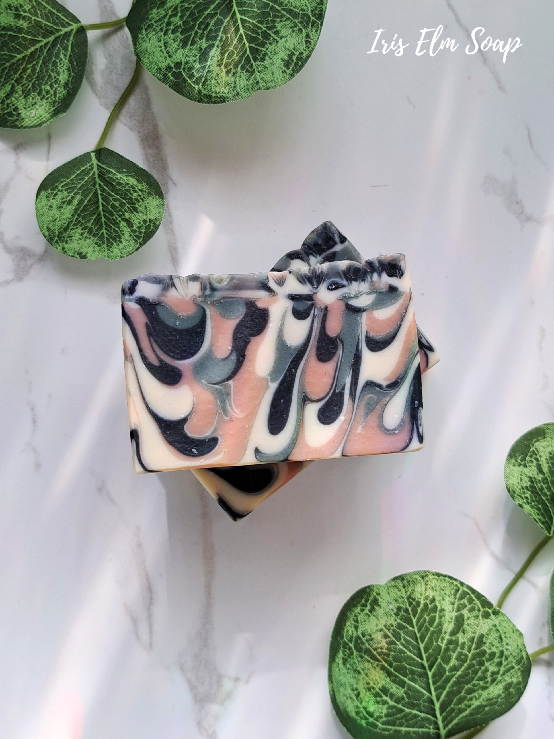 Swirled green tea handmade soap bar with black, white, and pink colors on a white background with green leaves.