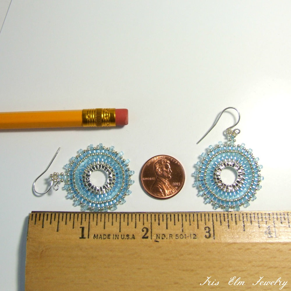 Two blue beaded earrings next to a penny and a ruler on a white background
