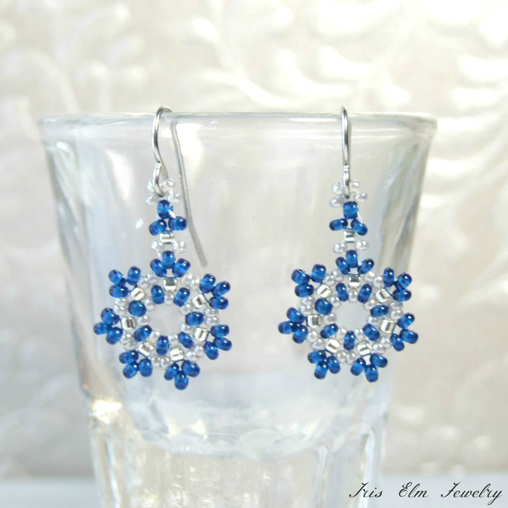 Cobalt blue and white beaded snowflake earrings on a clear glass with a white background