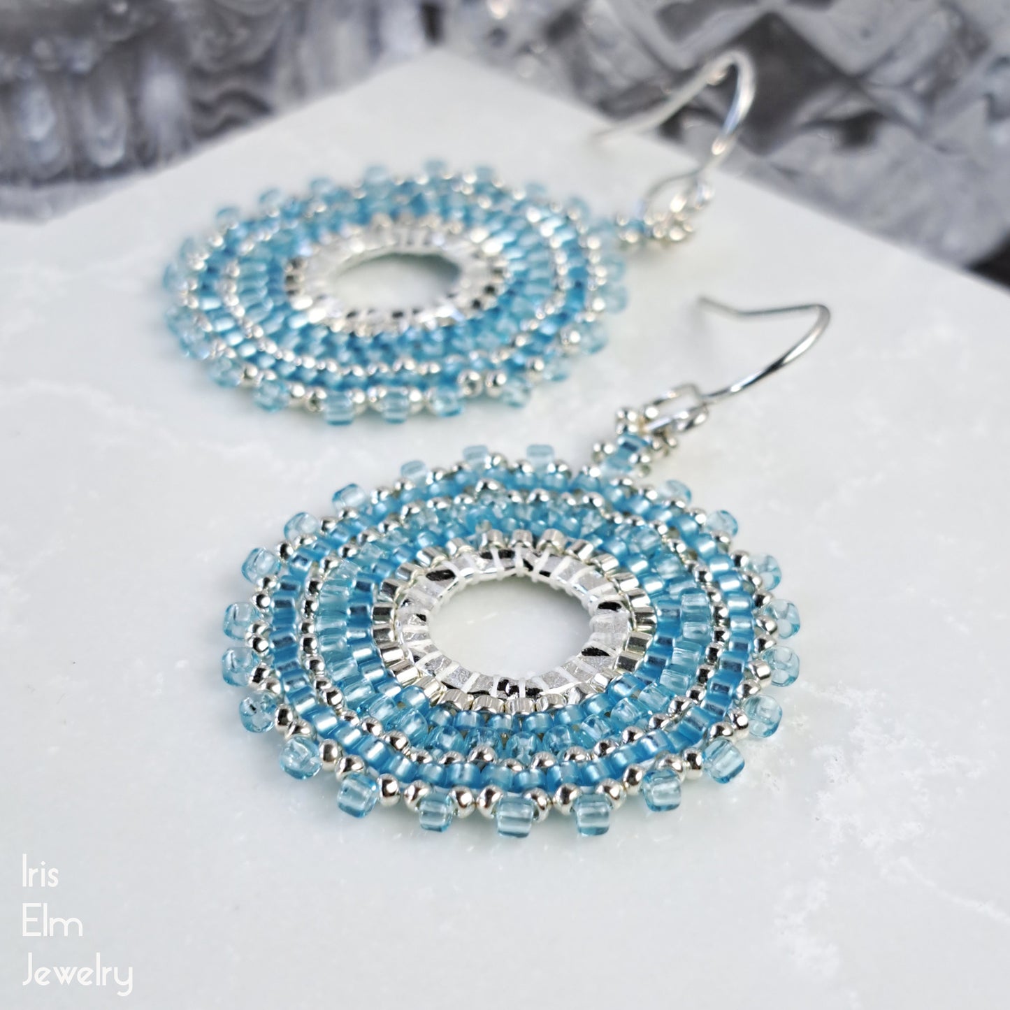 handcrafted light Blue beaded seed bead hoop earrings on a white surface with 'Iris Elm Jewelry' branding.