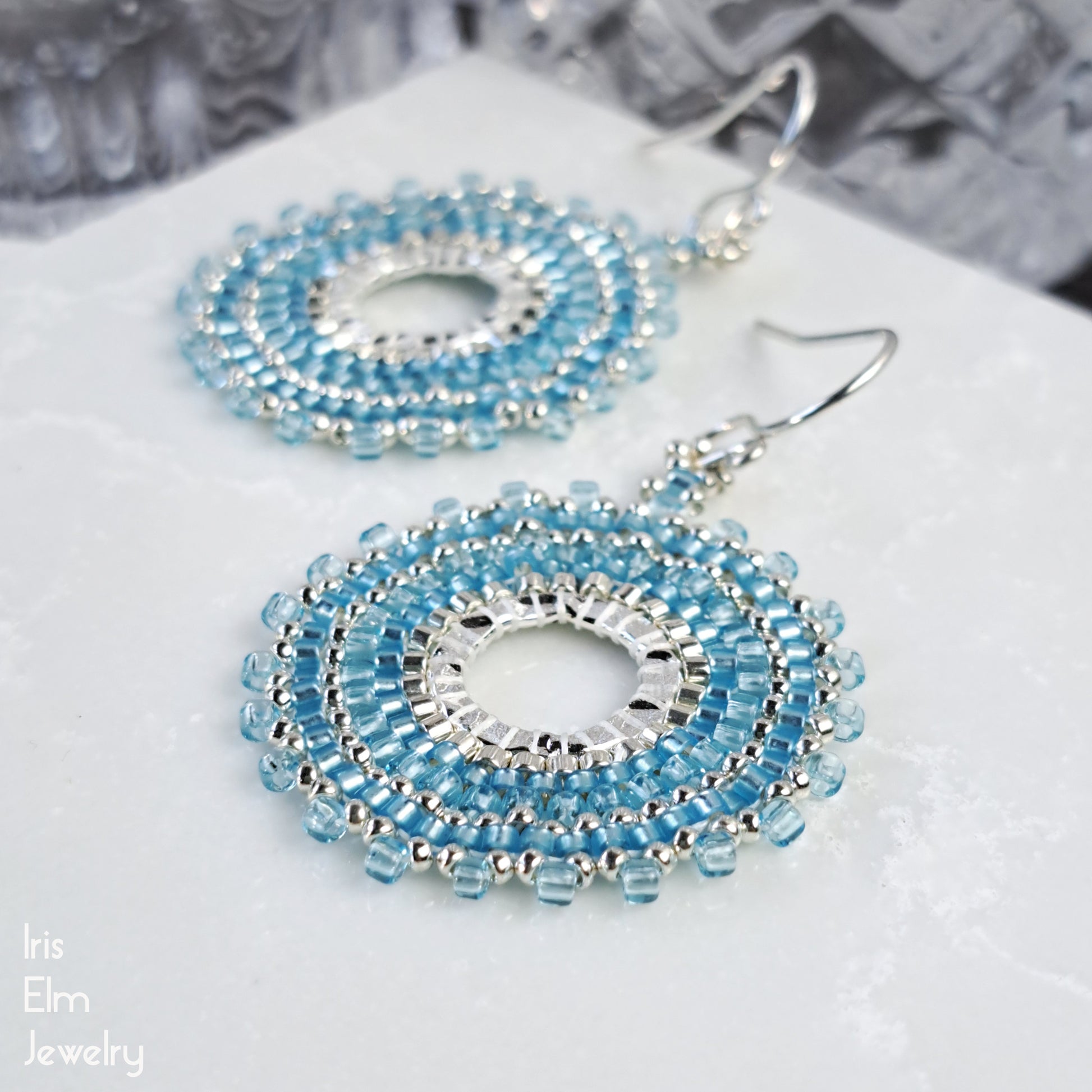 handcrafted light Blue beaded seed bead hoop earrings on a white surface with 'Iris Elm Jewelry' branding.
