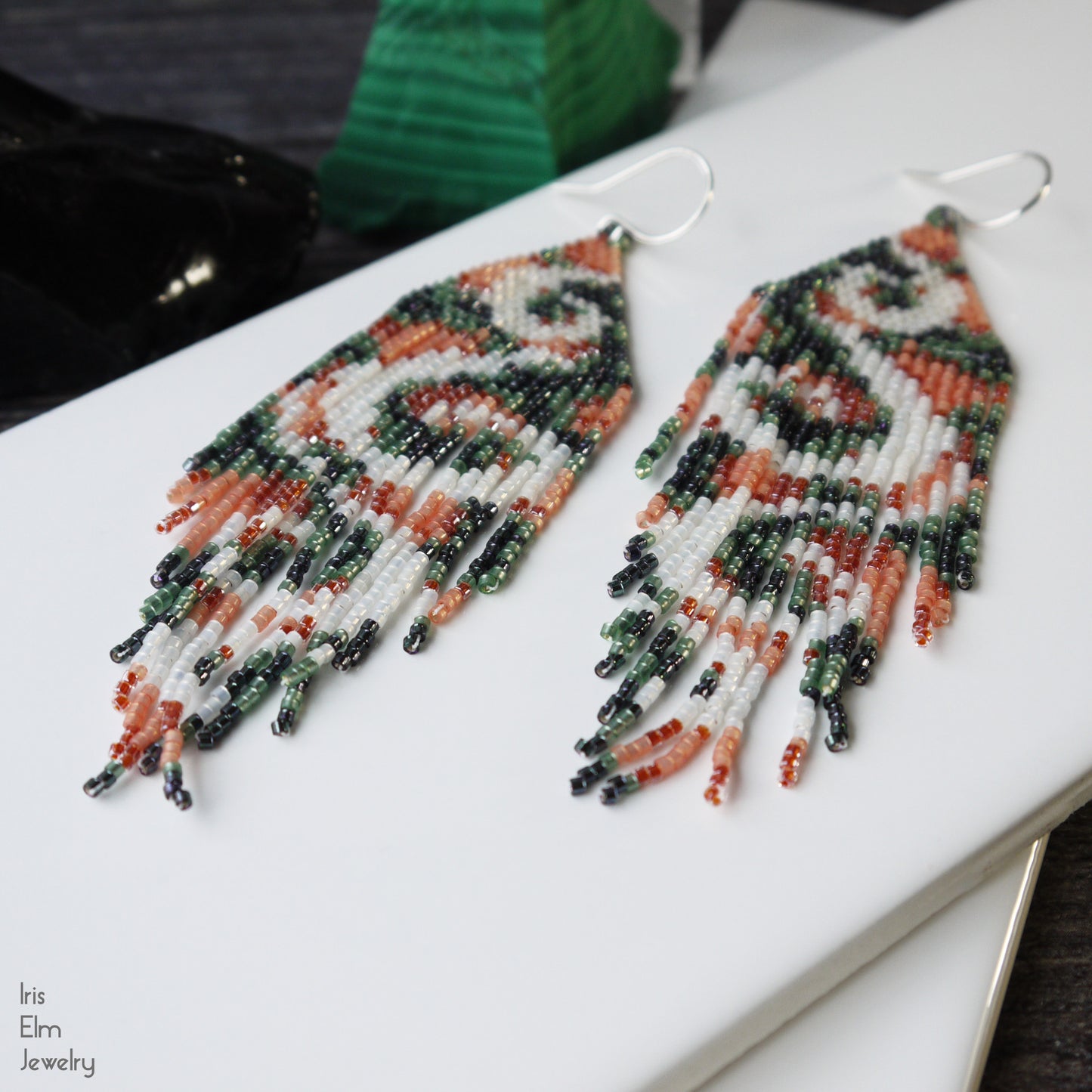handmade beadwork peach green and white seed bead fringe swirl earrings on a white surface with 'Iris Elm Jewelry' branding.