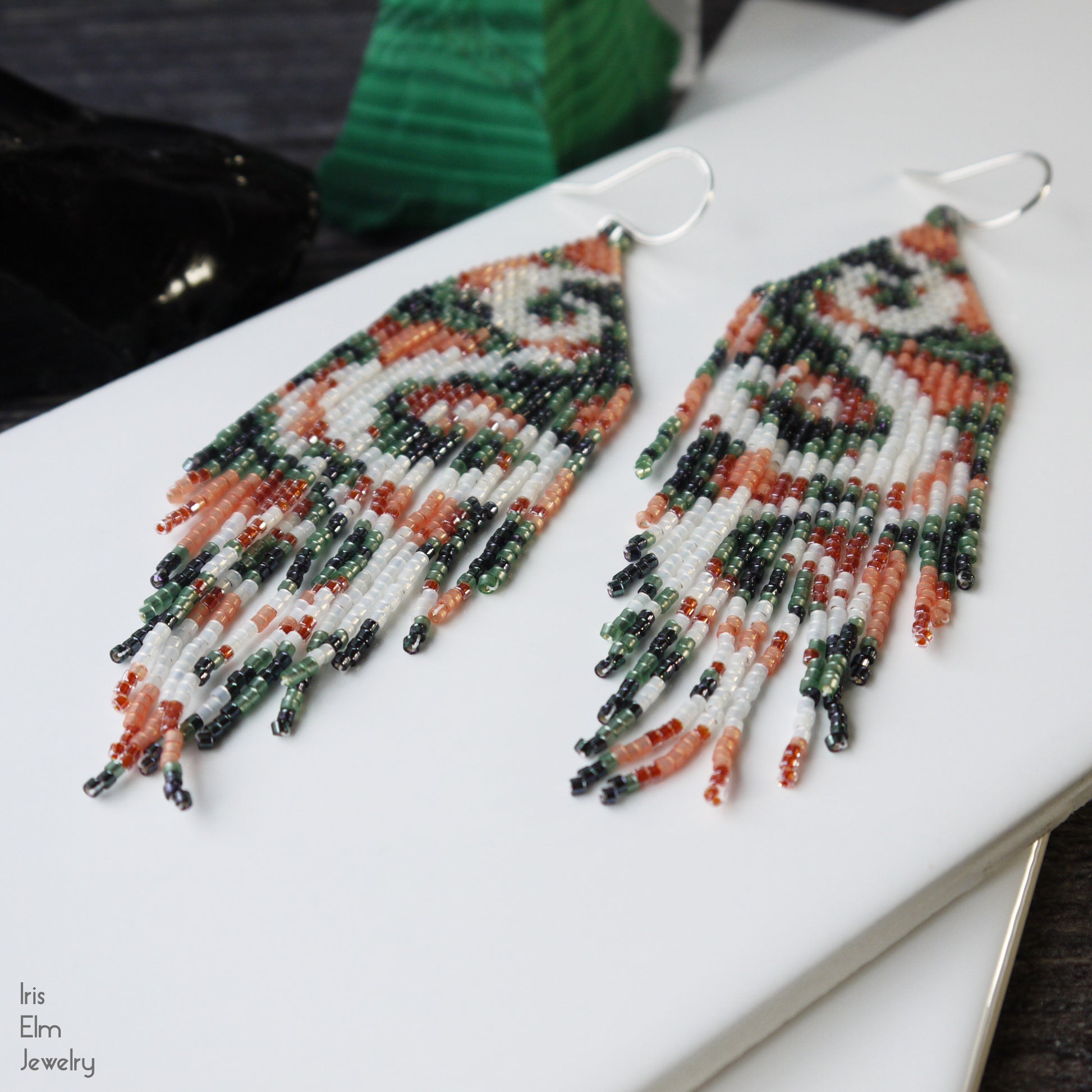 handmade beadwork peach green and white seed bead fringe swirl earrings on a white surface with 'Iris Elm Jewelry' branding.