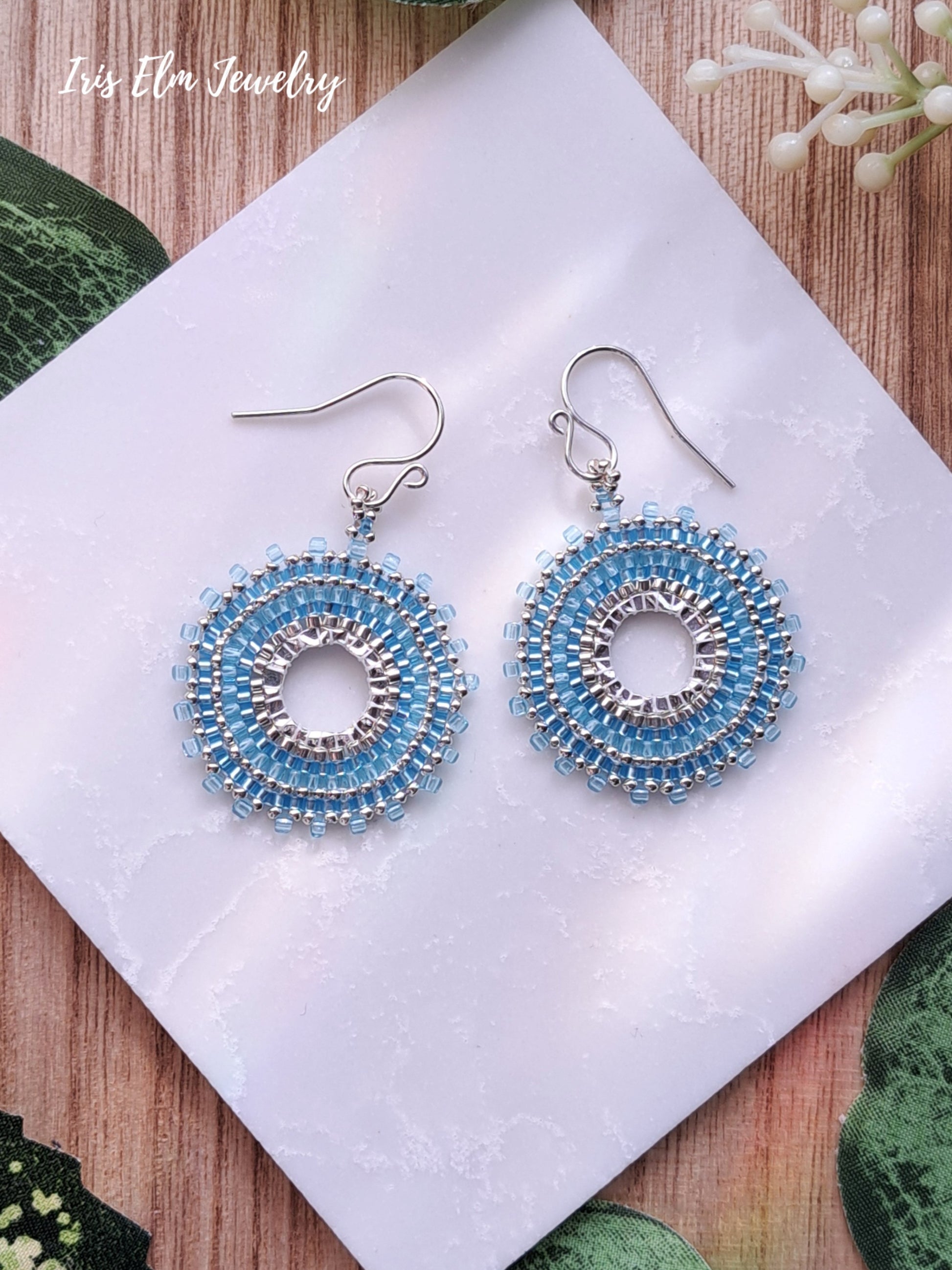 light Blue beaded seed bead woven hoop earrings on a white card with 'Iris Elm Jewelry' branding.