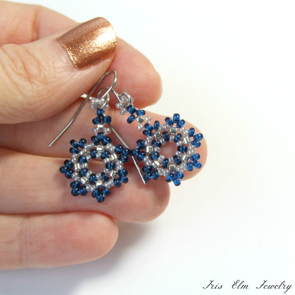 Beaded snowflake seed bead earrings held between fingers on a white background with 'Iris Elm Jewelry' branding.