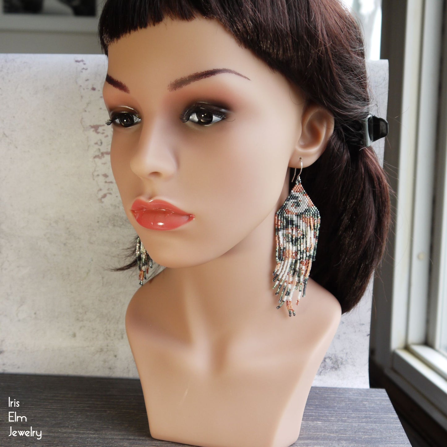 Mannequin head wearing a pair of long beaded fringe earrings with a neutral background.