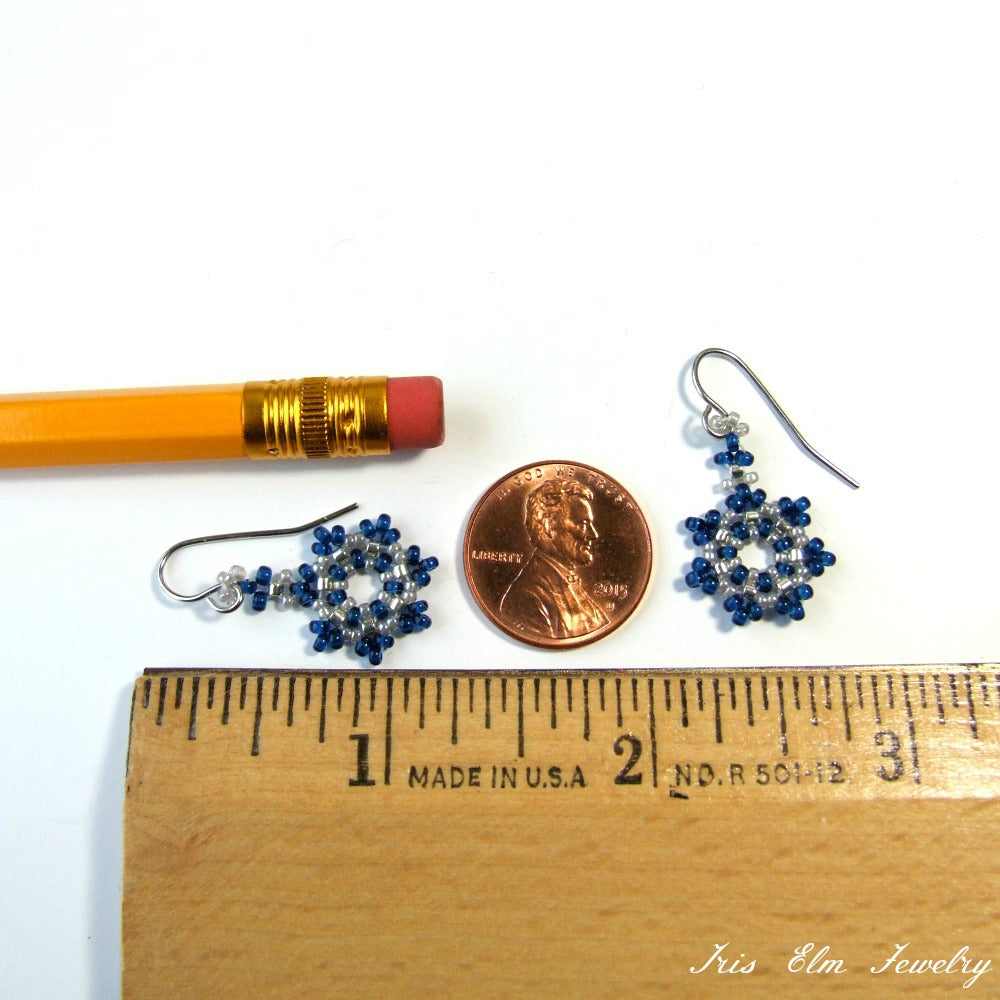 Pair of blue beaded seed bead snowflake earrings next to a penny and ruler for size comparison on a white background.