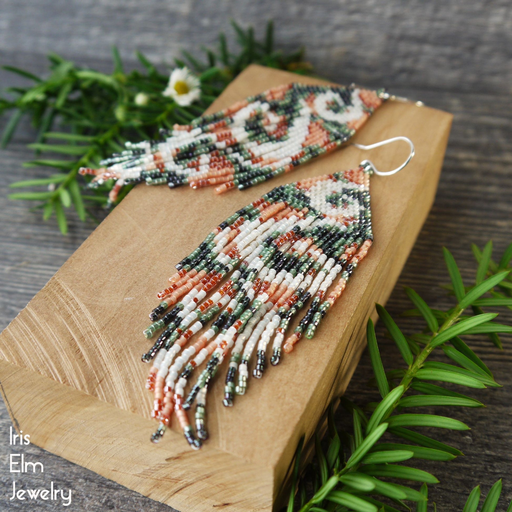 beadwork green, peach, and white seed bead fringe earrings with swirl design on a wooden board with greenery