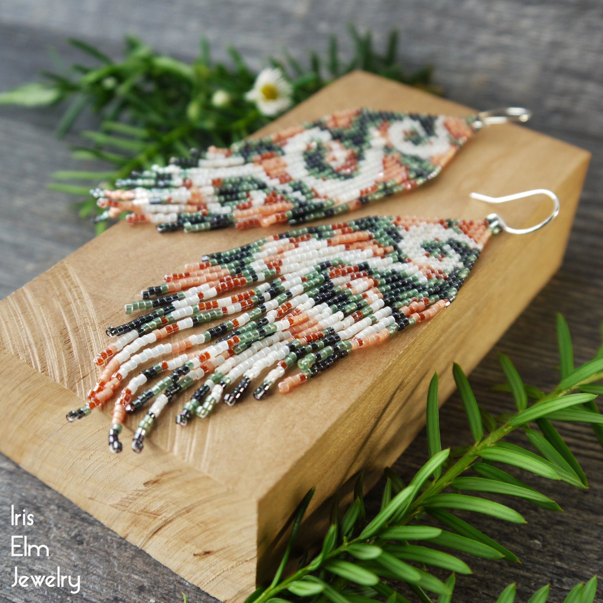 Beaded swirl long fringe seed bead glass earrings on a wooden board with greenery