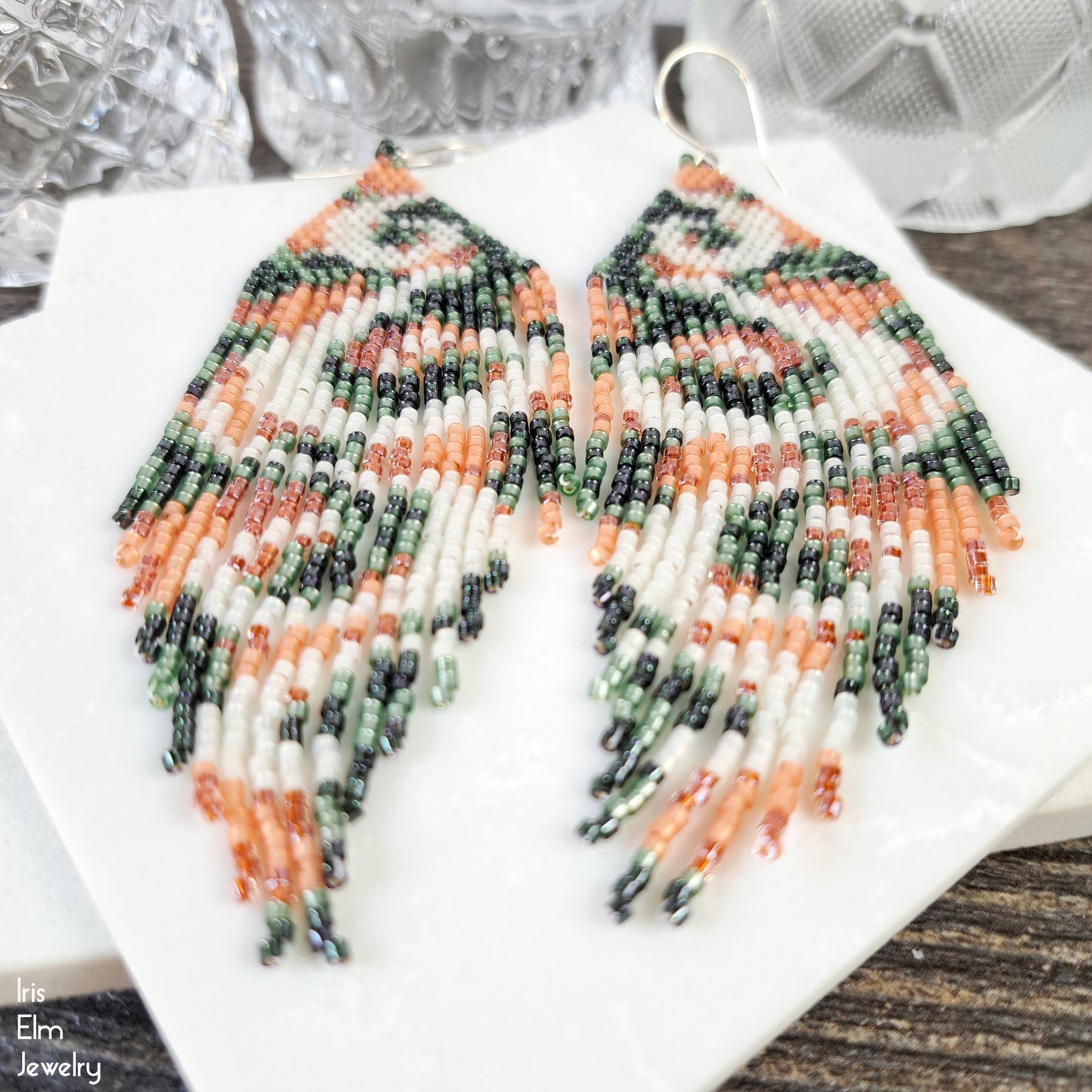 Beaded long fringe peach and green seed bead earrings with white swirl design on a white surface with 'Iris Elm Jewelry' branding.