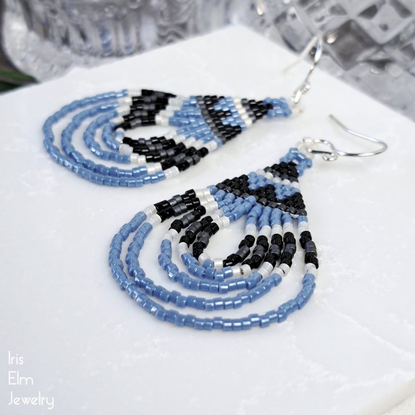 Beaded handmade earrings with blue, black, and white beads on a white surface.