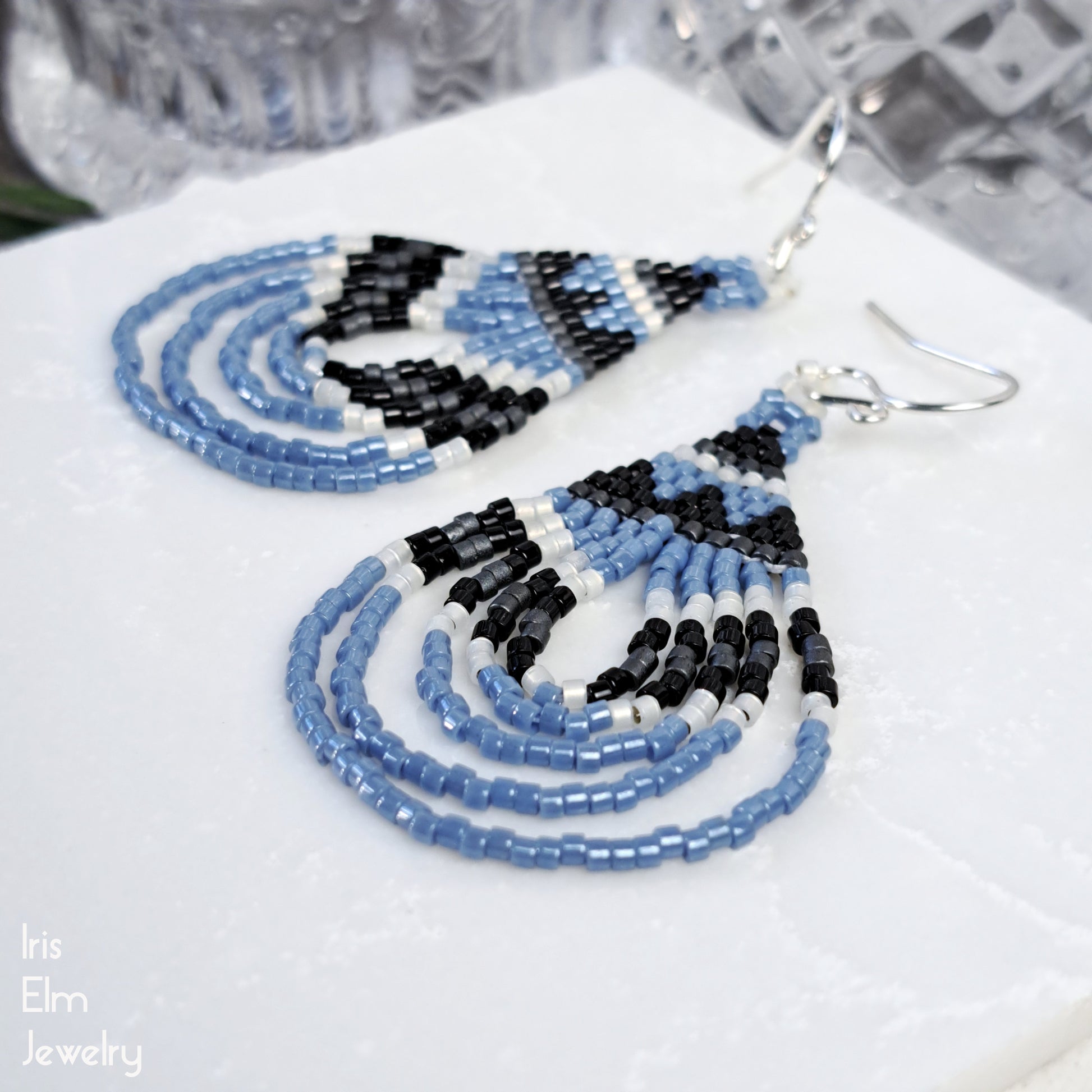 Beaded handmade earrings with blue, black, and white beads on a white surface.