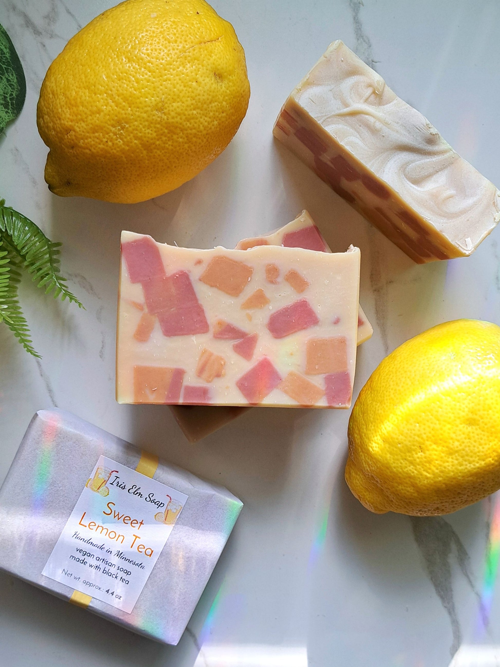 Three bars of sweet lemon tea handmade soap with visible branding next to two lemons on a light surface.