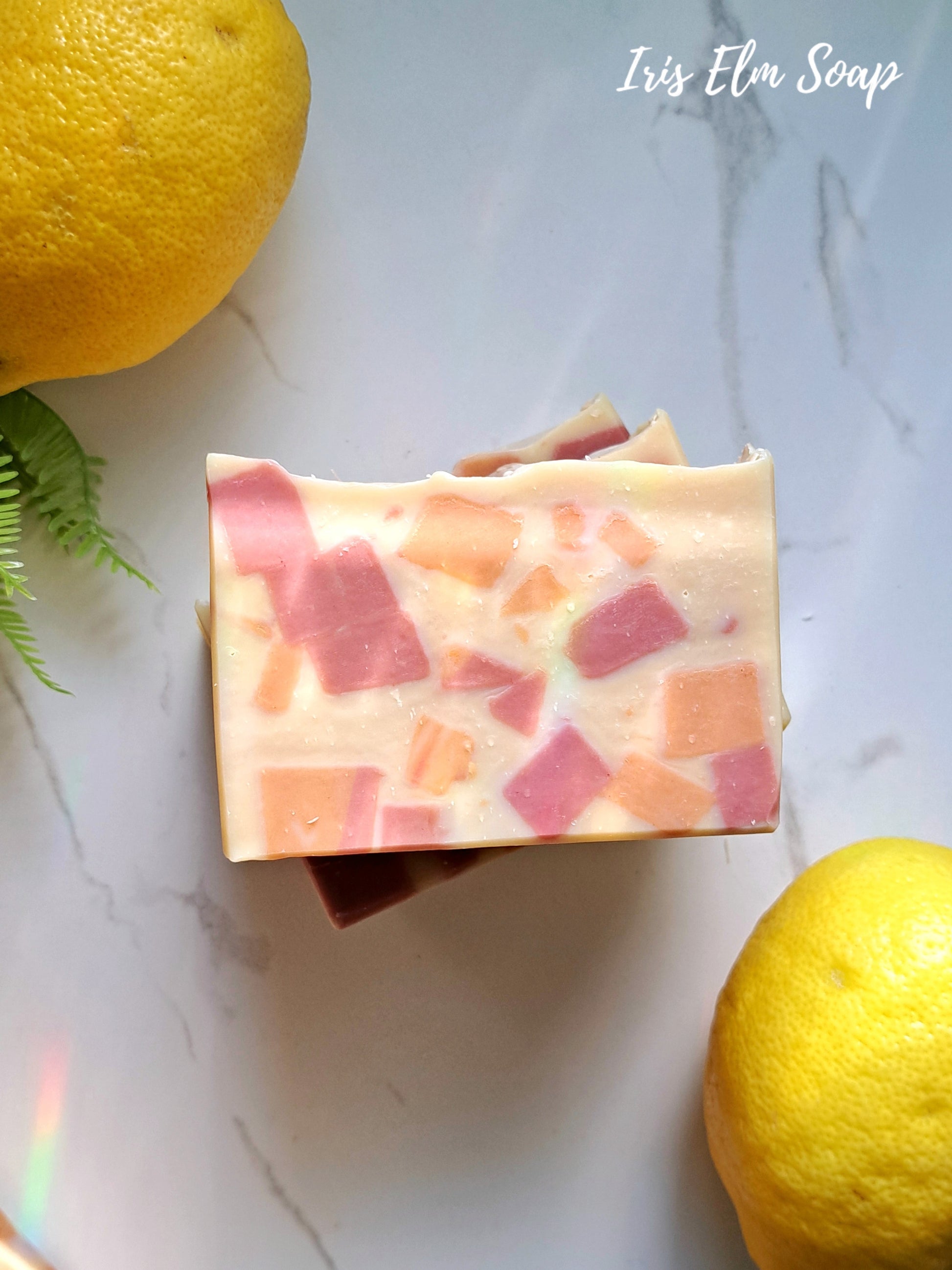 Bar of sweet lemon tea handmade soap with pink and orange clay pieces on a marble surface with lemons and greenery.