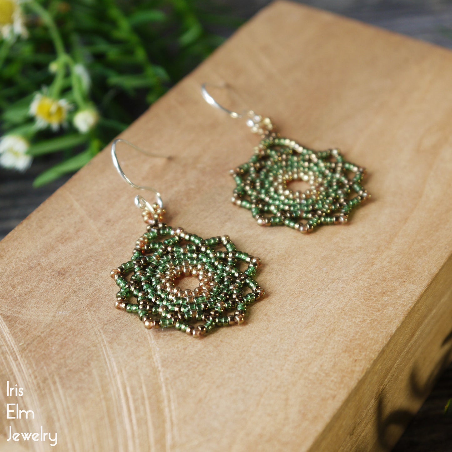 Green glass beaded circular mandala earrings on a wooden block with 'Iris Elm Jewelry' branding.