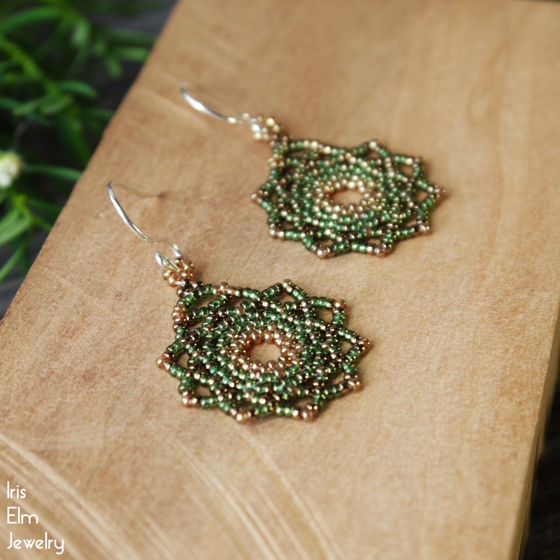 Green beaded handmade mandala seed bead earrings on a wooden surface with 'Iris Elm Jewelry' branding.