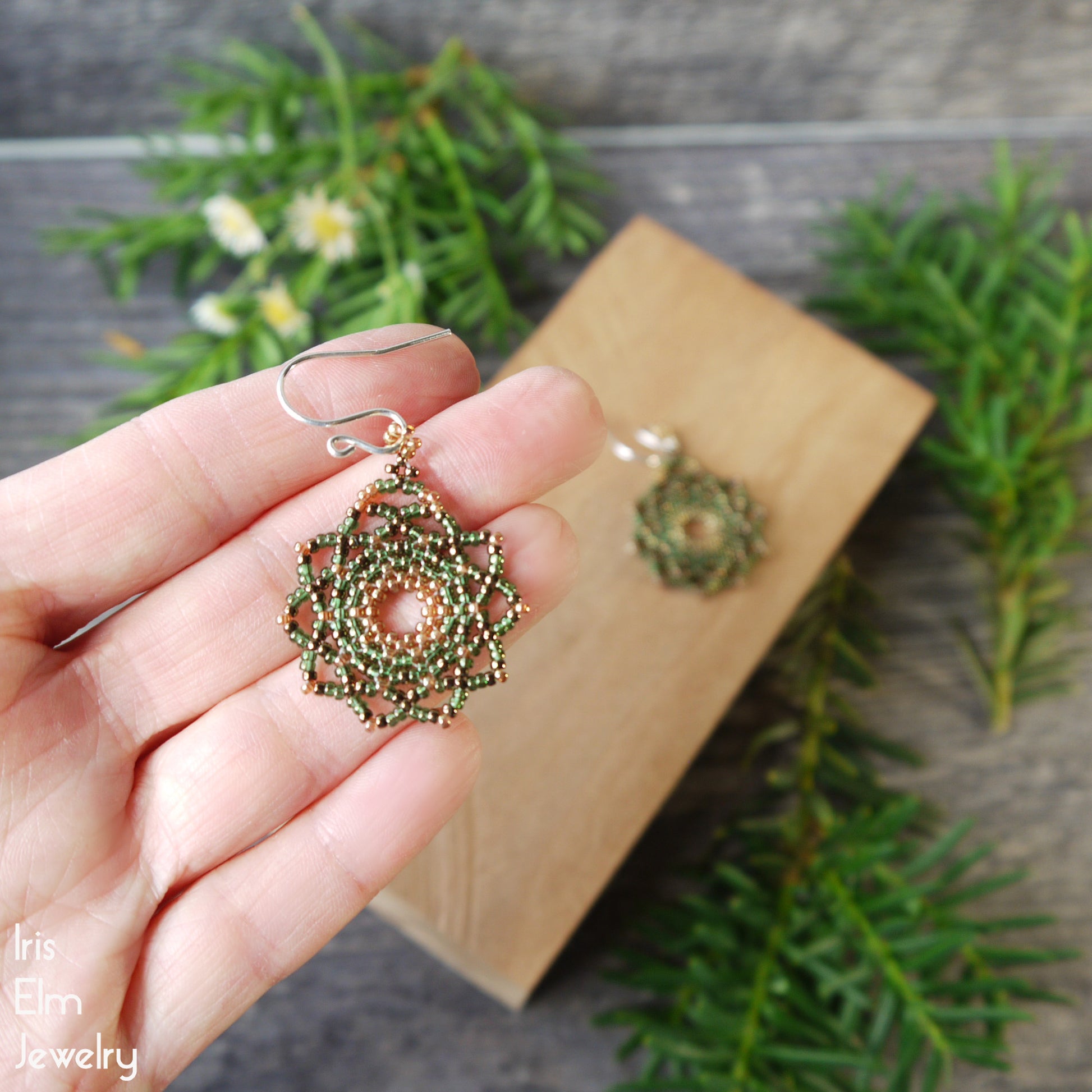 Green woven mandala beaded earrings held in a hand with a natural background