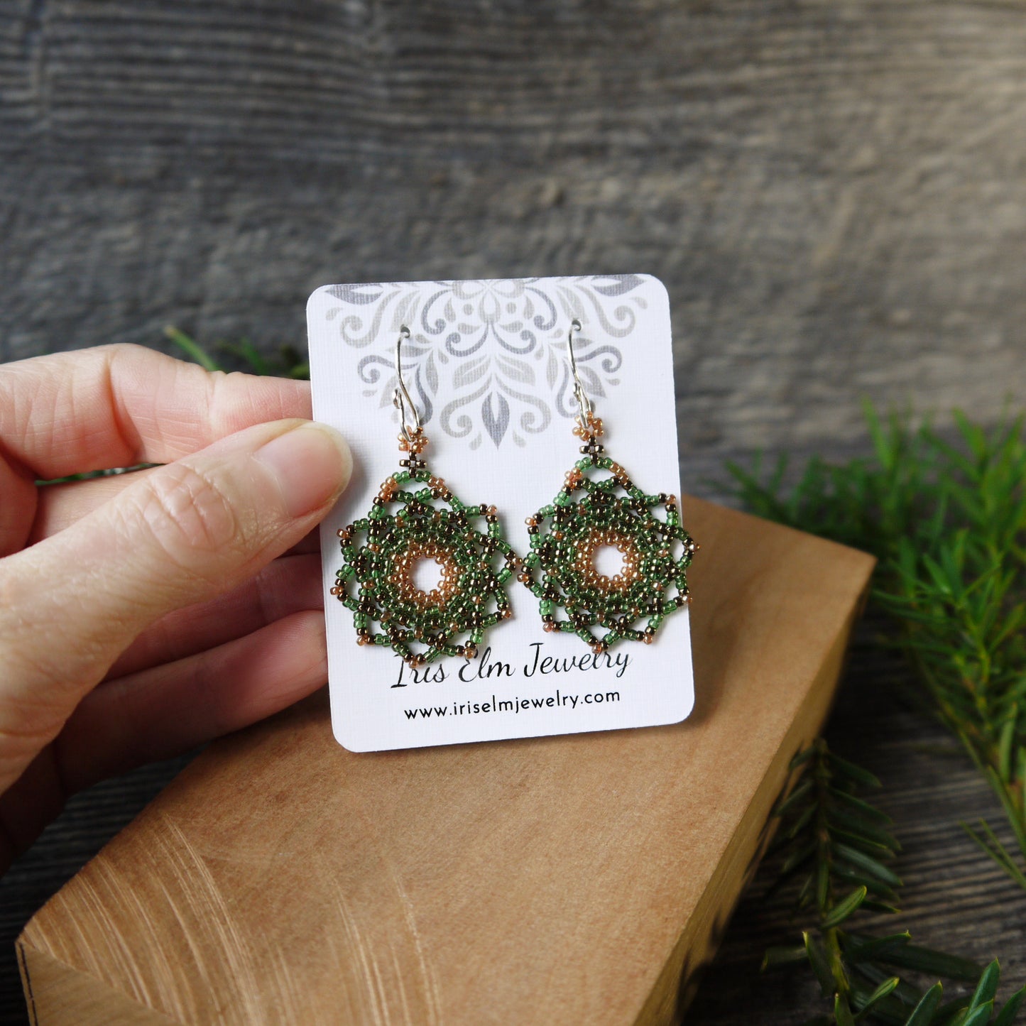 Green beaded earrings on a card held by a hand with a natural background