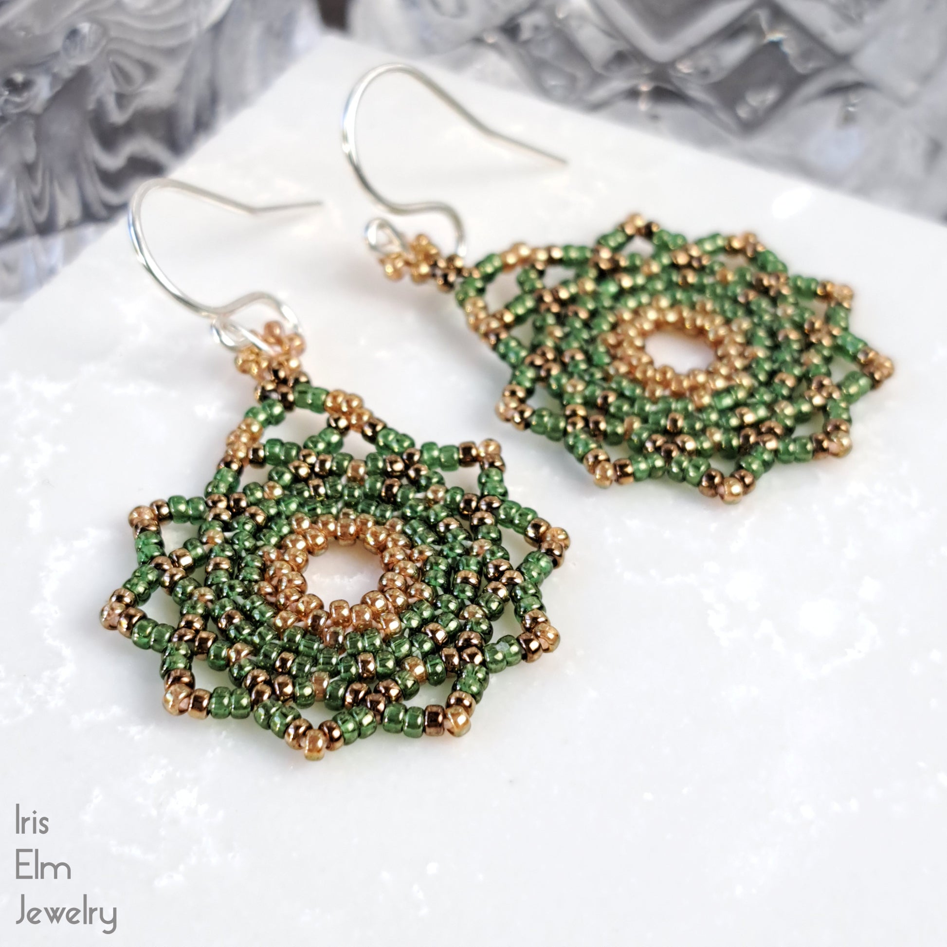 Green and golden mandala handcrafted beaded earrings on a white surface with 'Iris Elm Jewelry' branding.