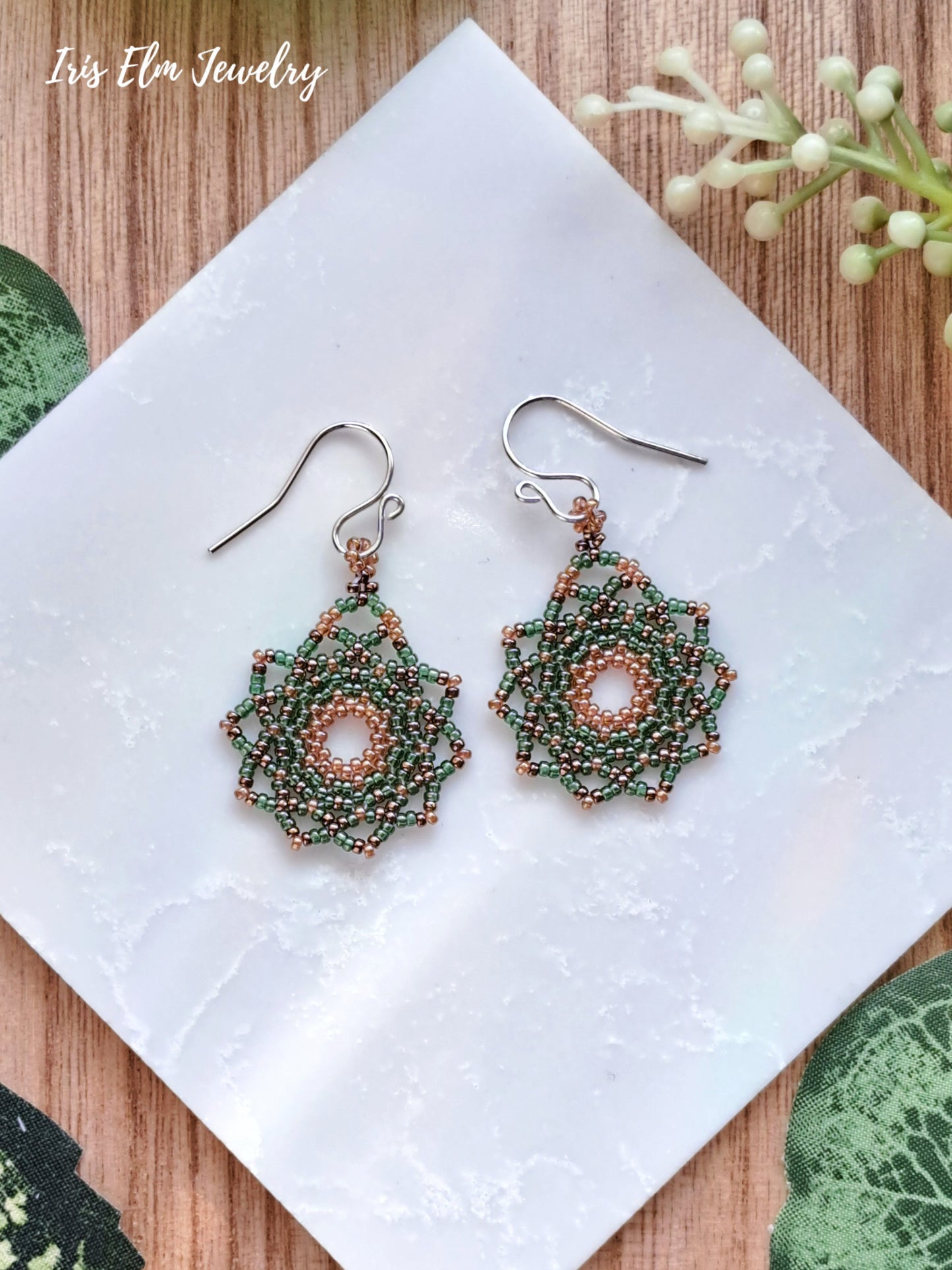 Pair of beaded green seed bead mandala earrings on a white napkin with 'Iris Elm Jewelry' branding.