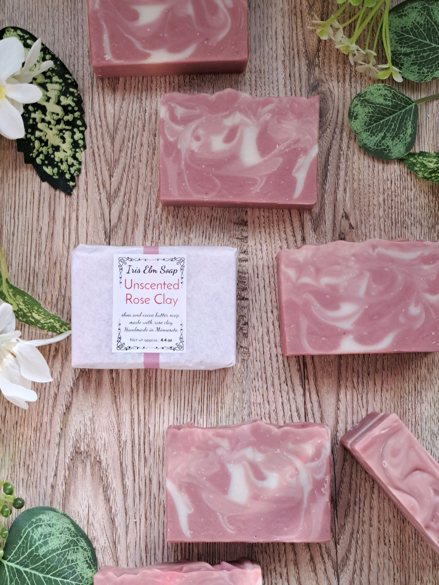 Pink marbled unscented rose clay handmade soap bars on a wooden surface with green leaves and flowers.