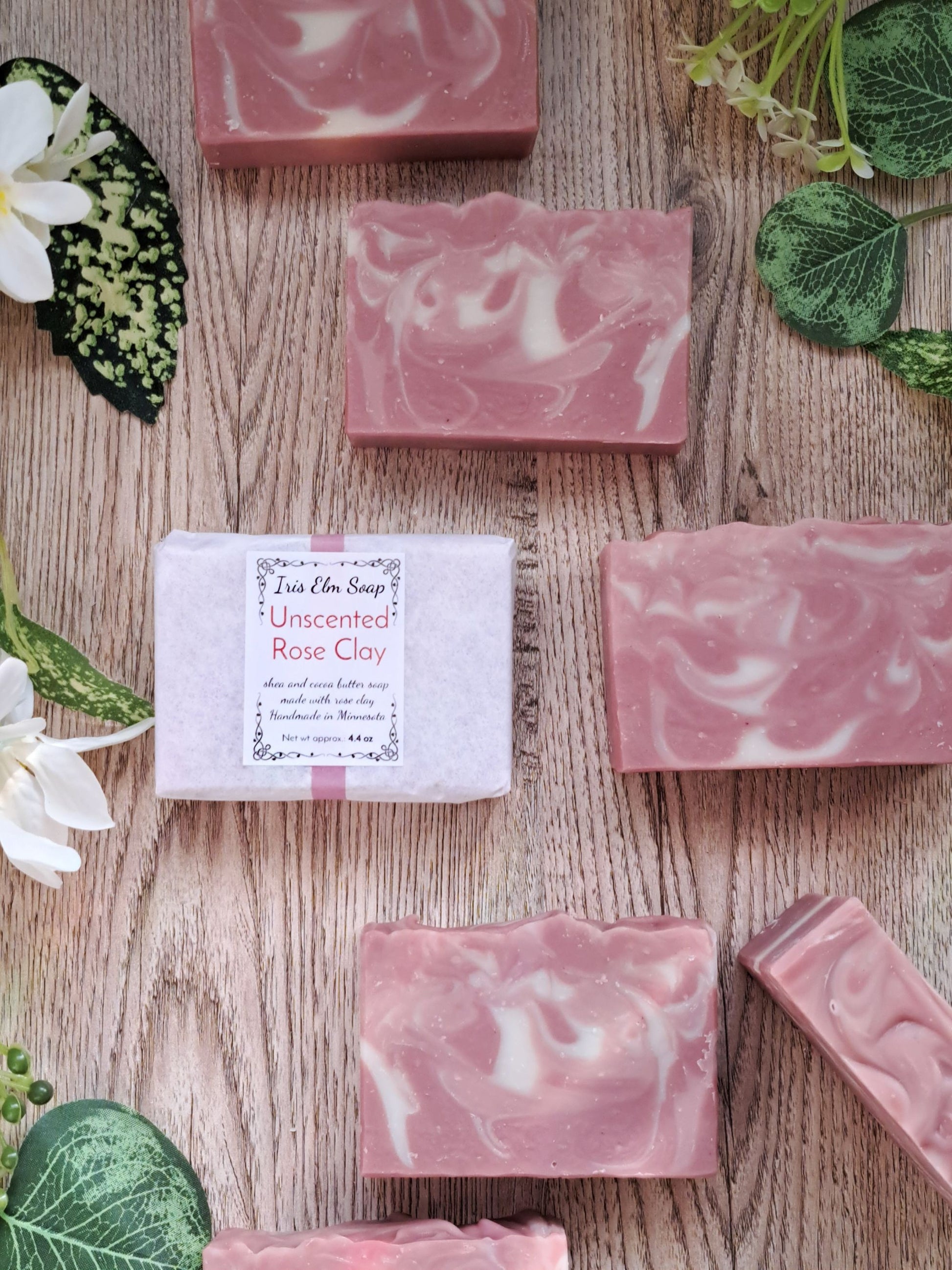 Pink marbled unscented rose clay handmade soap bars on a wooden surface with green leaves and flowers.