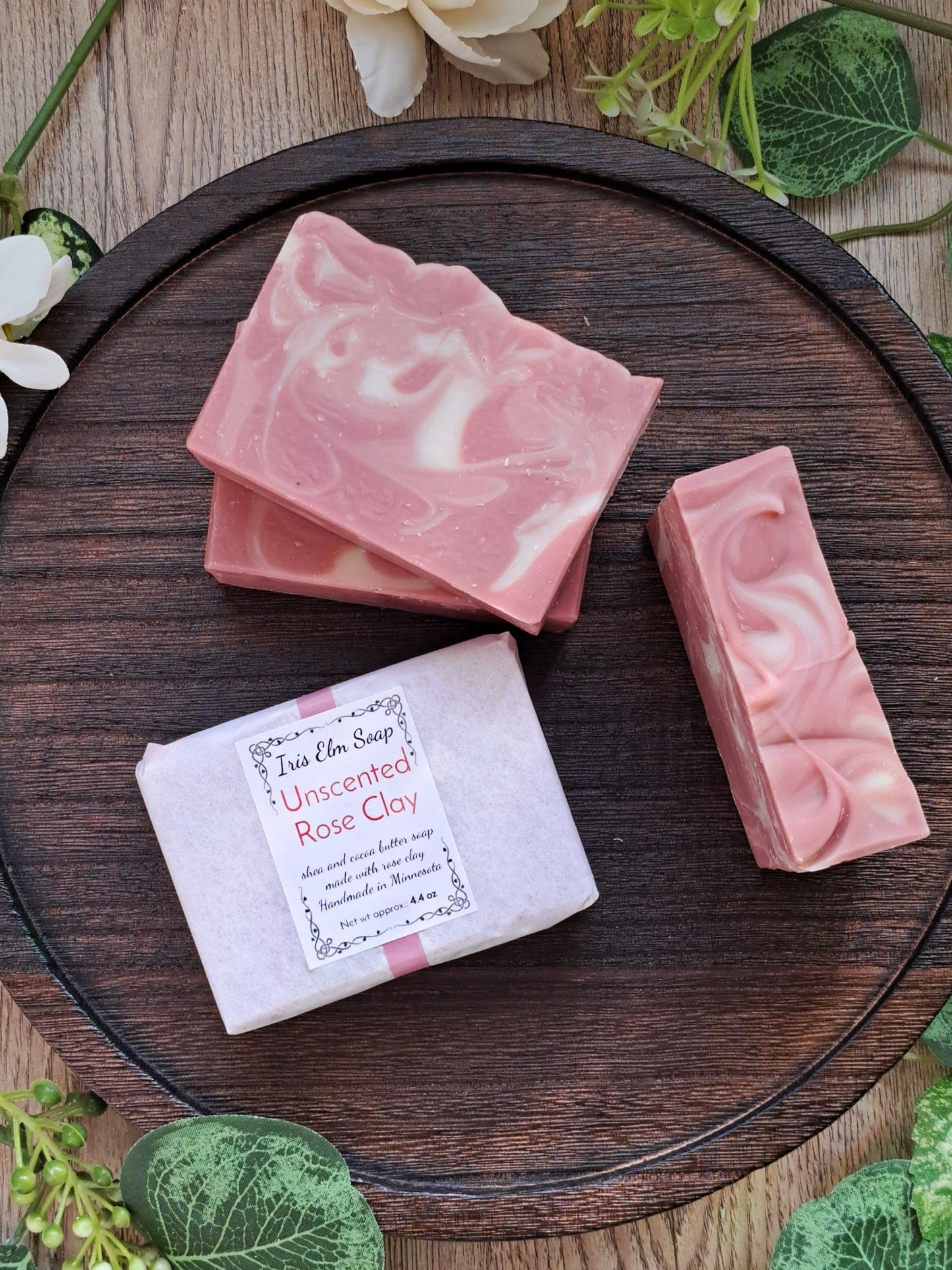 Pink unscented rose clay handmade soap bars on a wooden board with greenery around