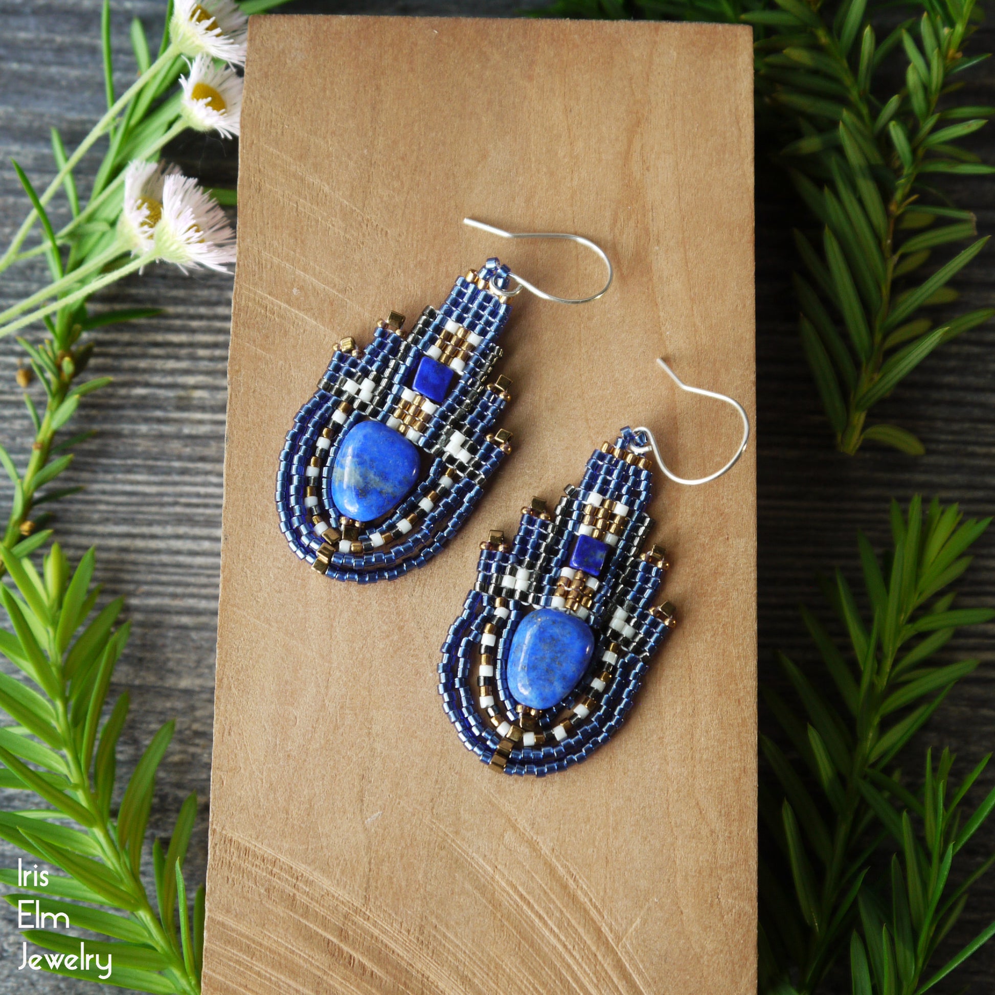 Blue lapis lazuli boho beaded earrings with seed beads and sterling silver ear wires on a wooden surface with greenery around