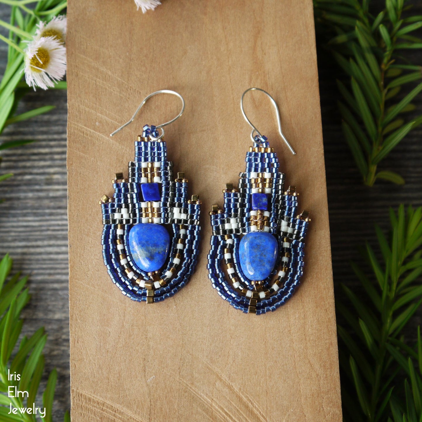 Blue lapis lazuli stone and seed bead handmade beaded earrings on a wooden surface with greenery in the background
