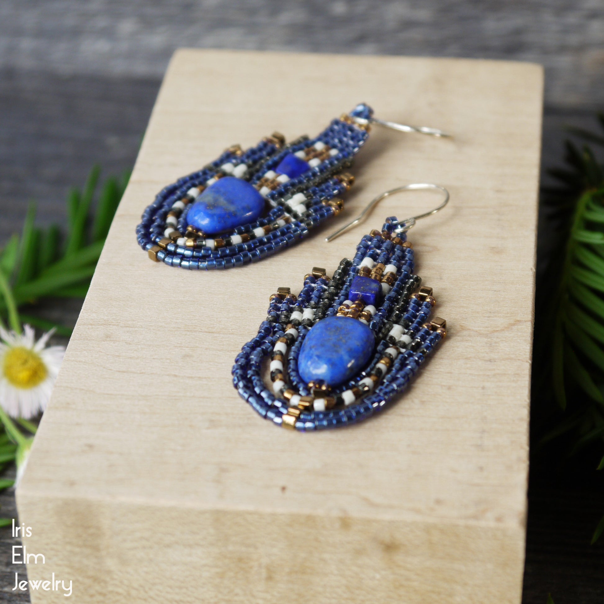 Blue lapis lazuli gemstone beaded seed bead teardrop earrings on a wooden block with 'Iris Elm Jewelry' branding.