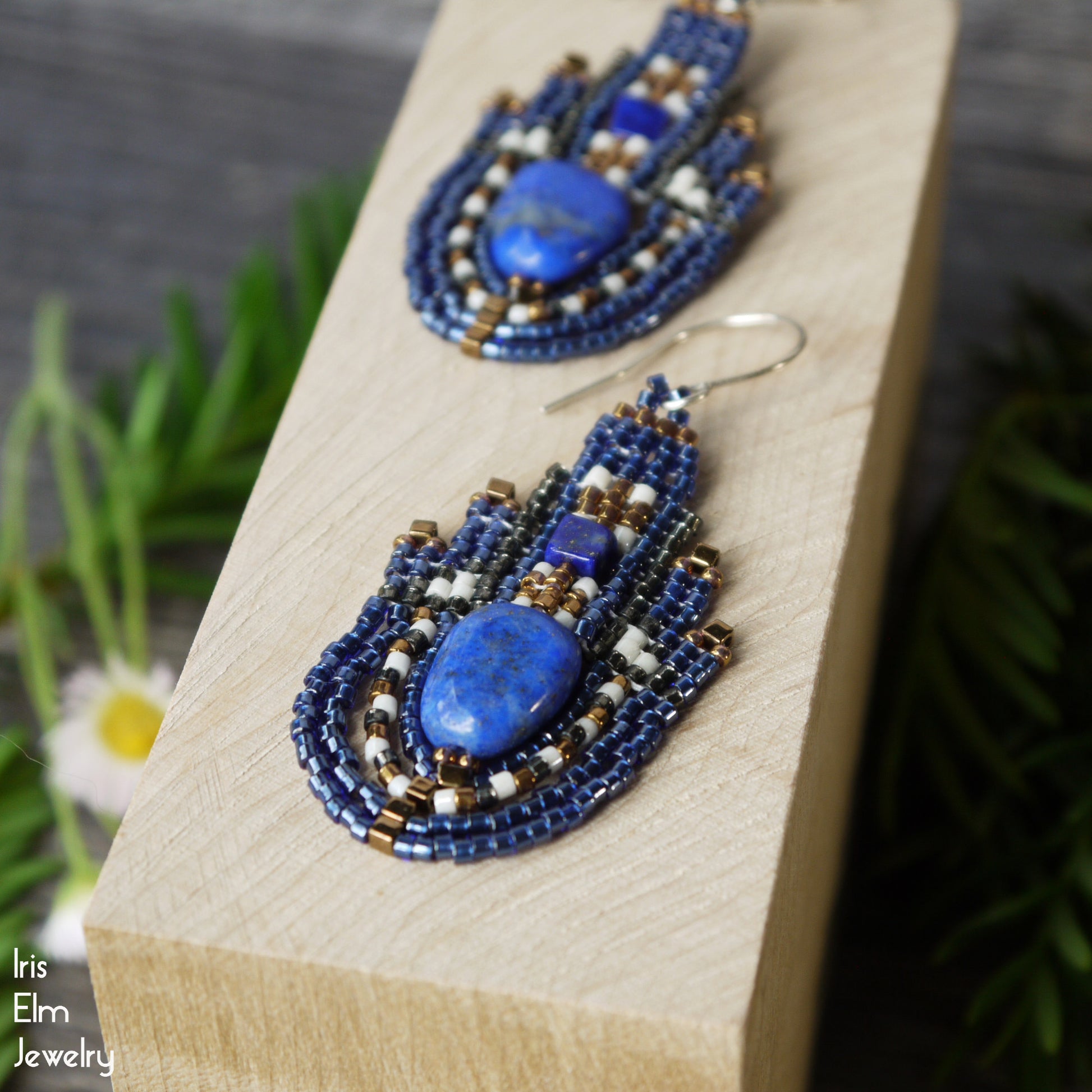 Blue lapis lazuli gemstone beadwork earrings on a wooden block with a natural background