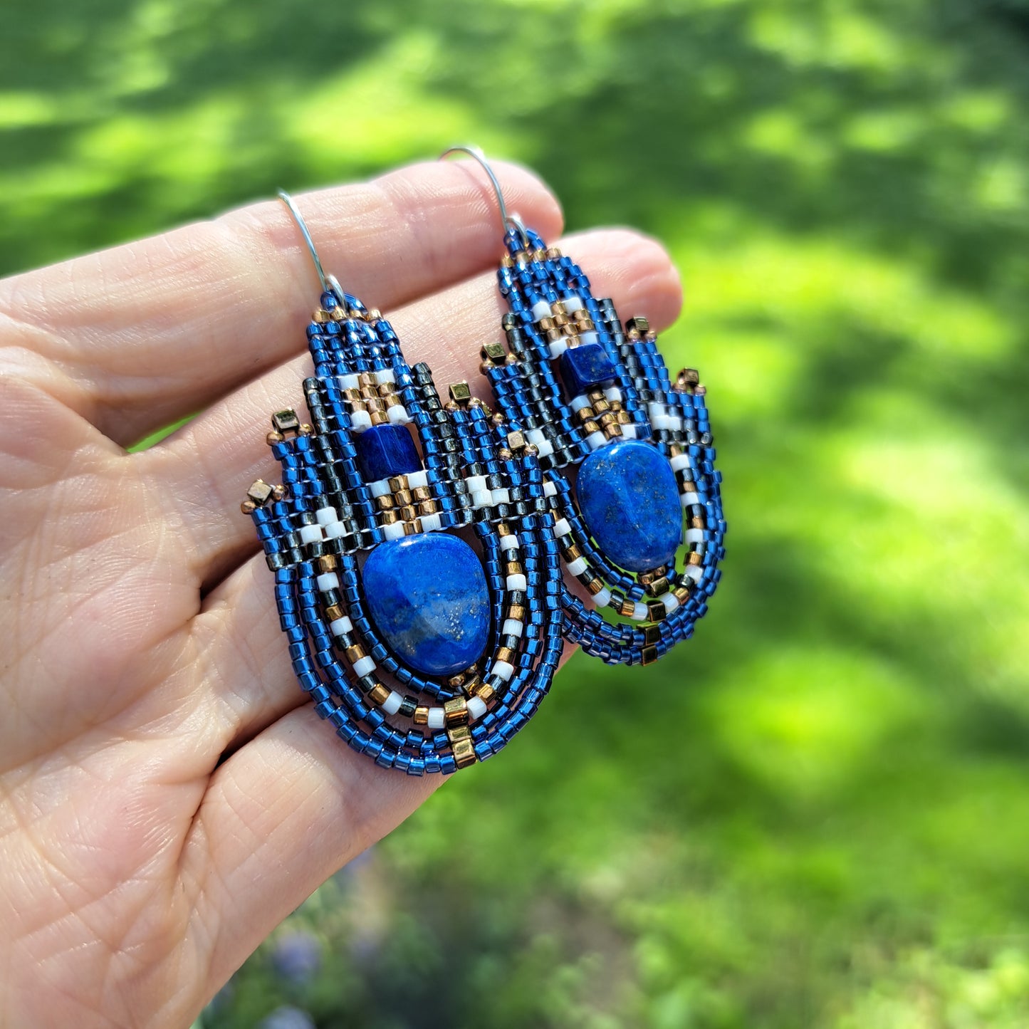 Blue lapis lazuli beadwork earrings held in a hand with a blurred green background