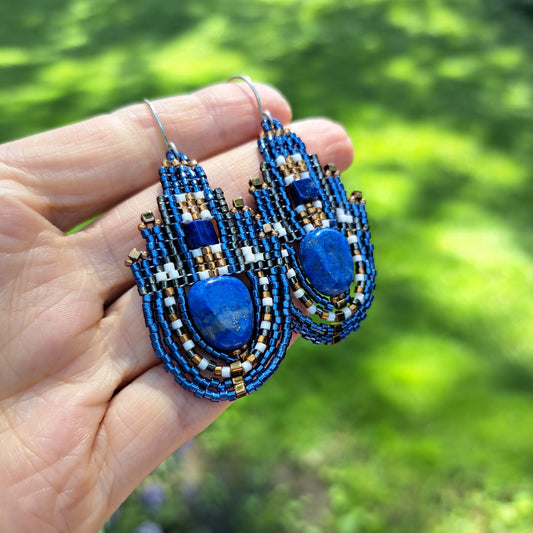Blue lapis lazuli beadwork earrings held in a hand with a blurred green background