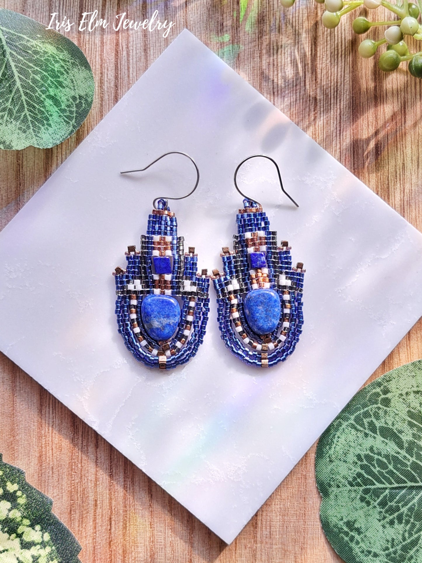 Blue beaded lapis lazuli earrings on a white tile with green leaves in the background