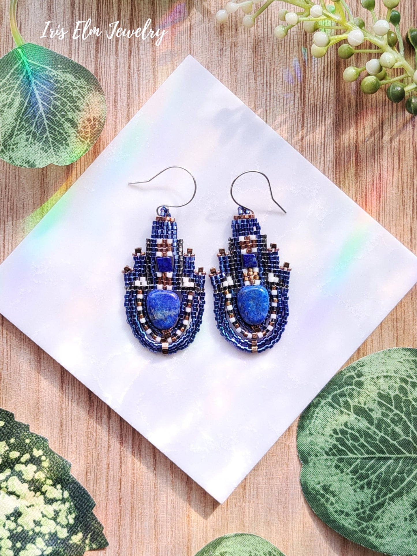 Blue beaded lapis lazuli teardrop earrings on a white napkin with green leaves in the background